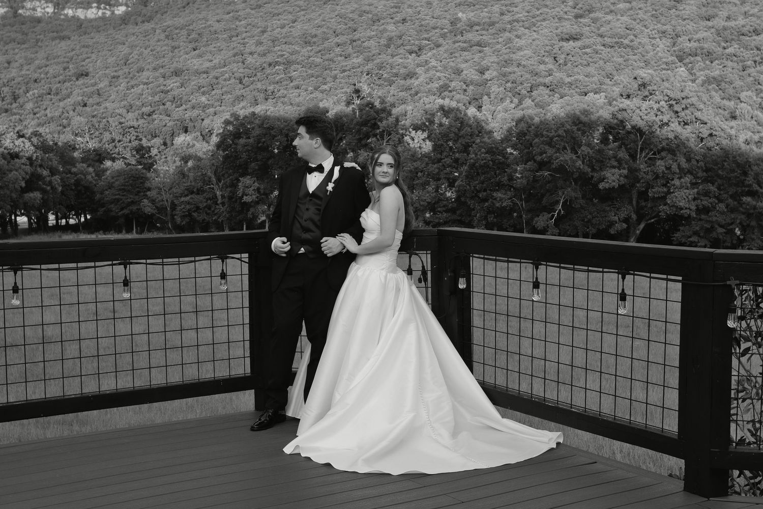 Black and white photo of a bride and groom sharing a romantic moment on a deck with mountain views.