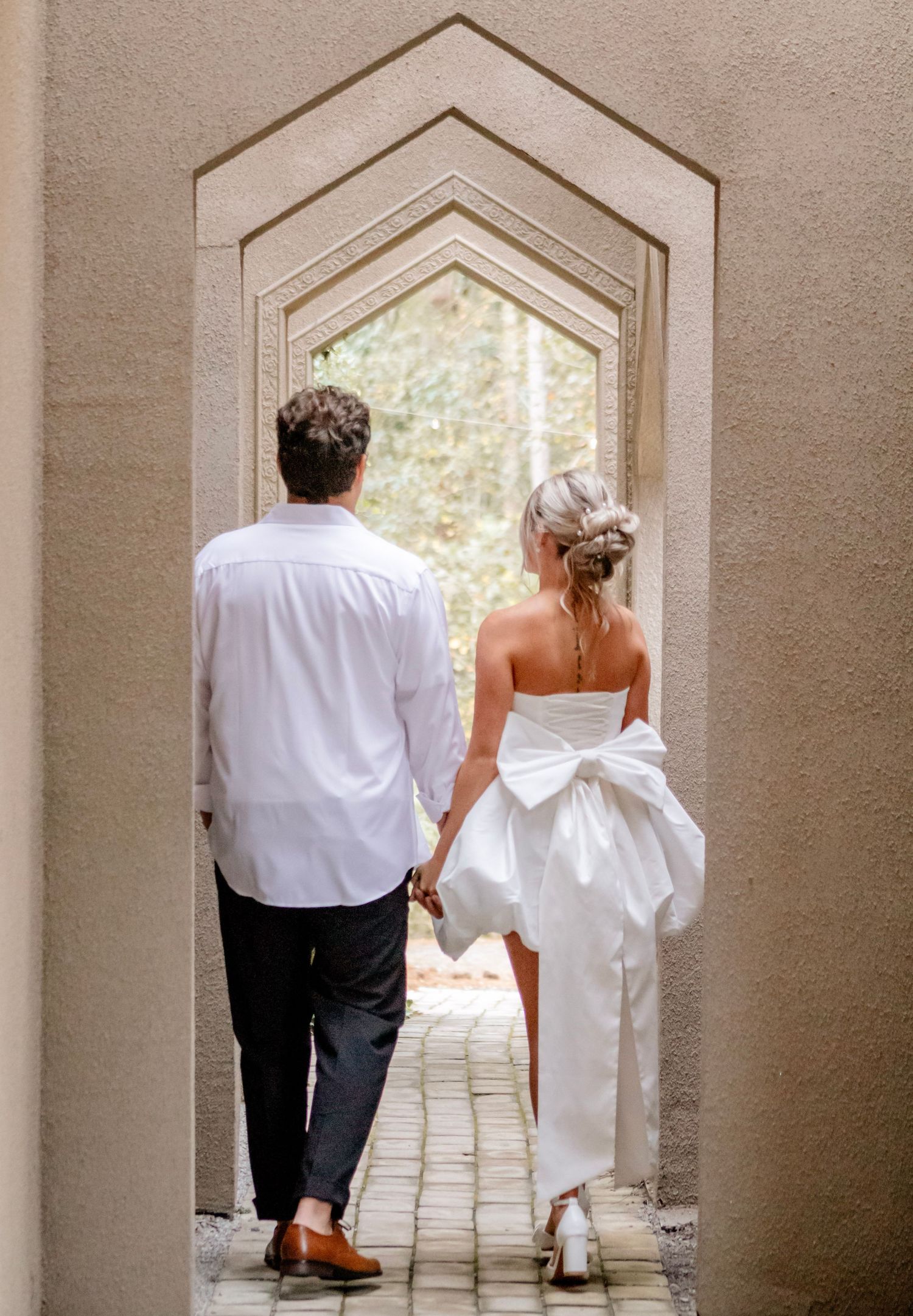 Wedding couple walking through architectural archways in elegant formal wear.