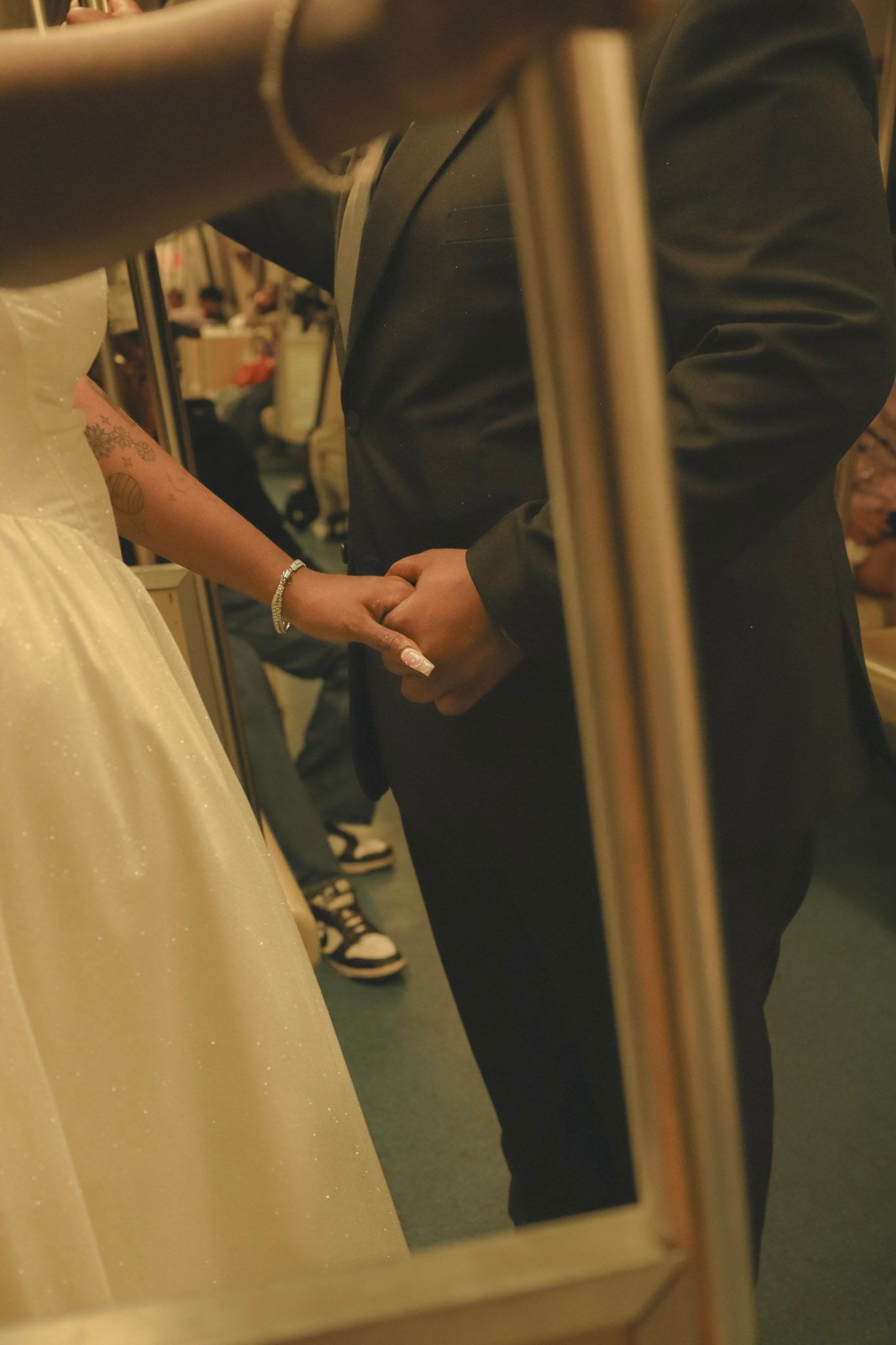 Bride and groom holding hands in wedding attire, reflected in a mirror, with sneakers visible beneath the suit.