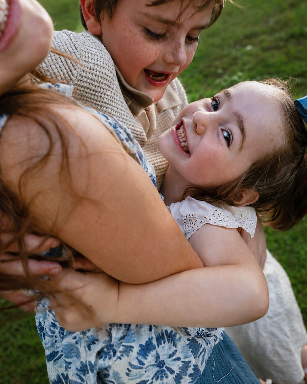 Two happy children laughing and hugging outdoors on green grass, wearing casual summer clothes.