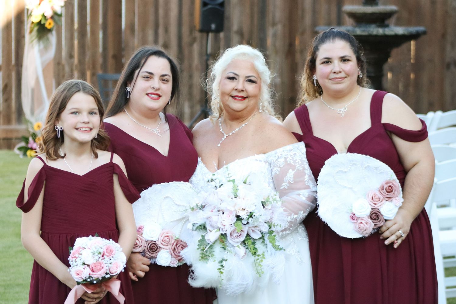 Bridal party in burgundy dresses and white bouquets poses together outdoors.