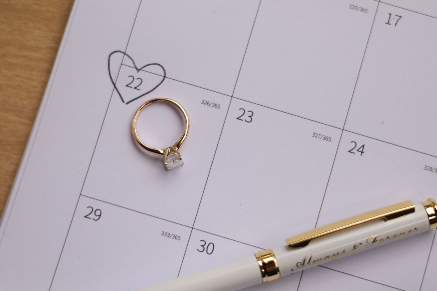 Wedding planning details with calendar, pen and ring on white background.