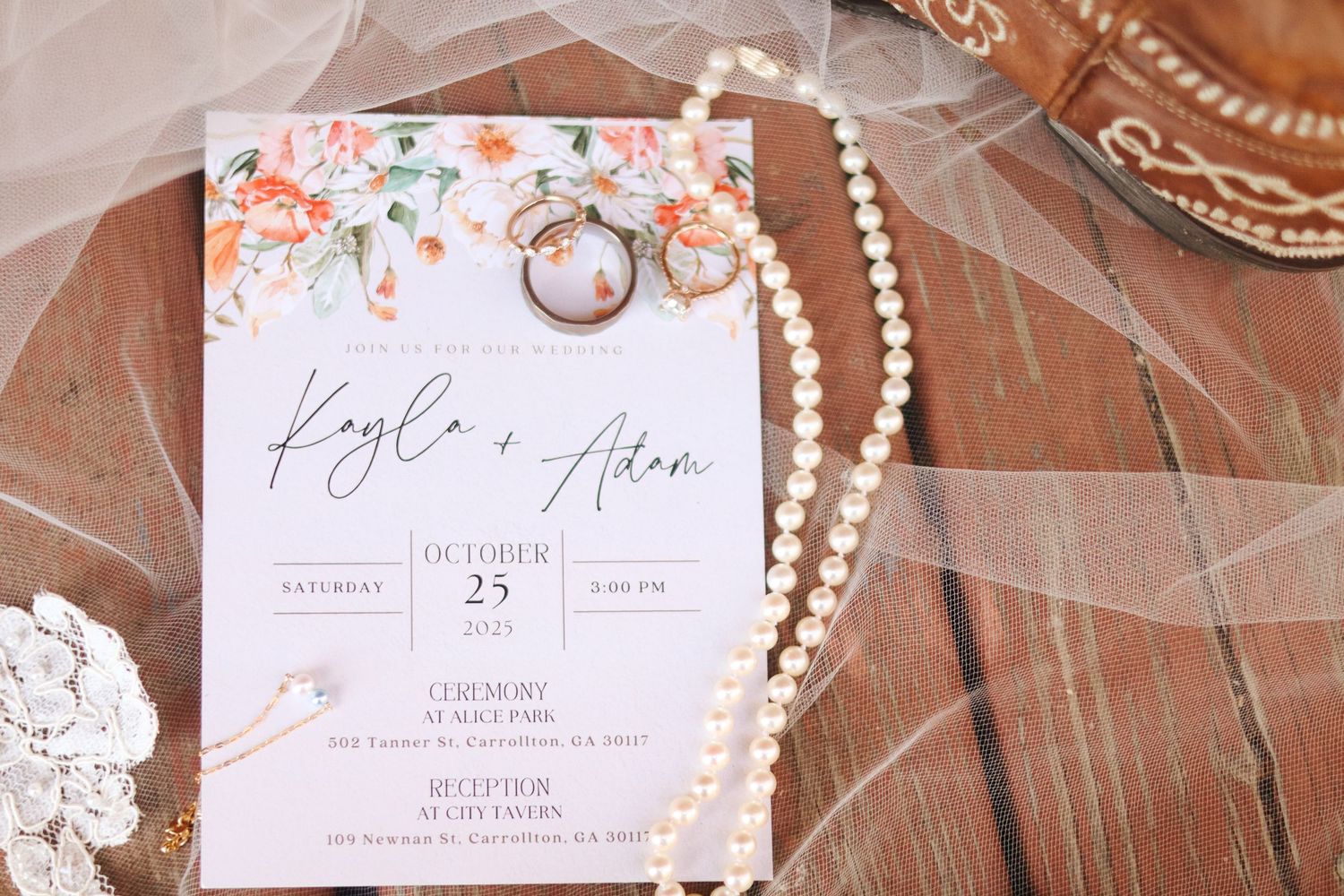 Wedding invitations with floral design and pearl necklace laid out on terracotta tiles.