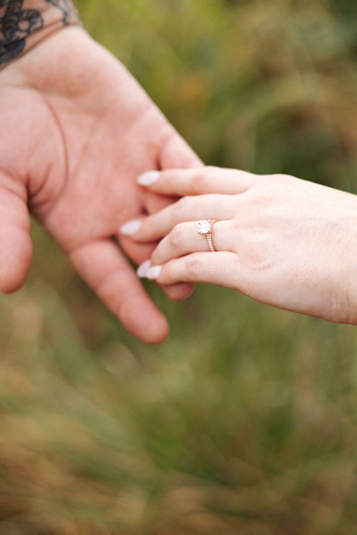 Close up of hands reaching for each other with engagement ring visible.
