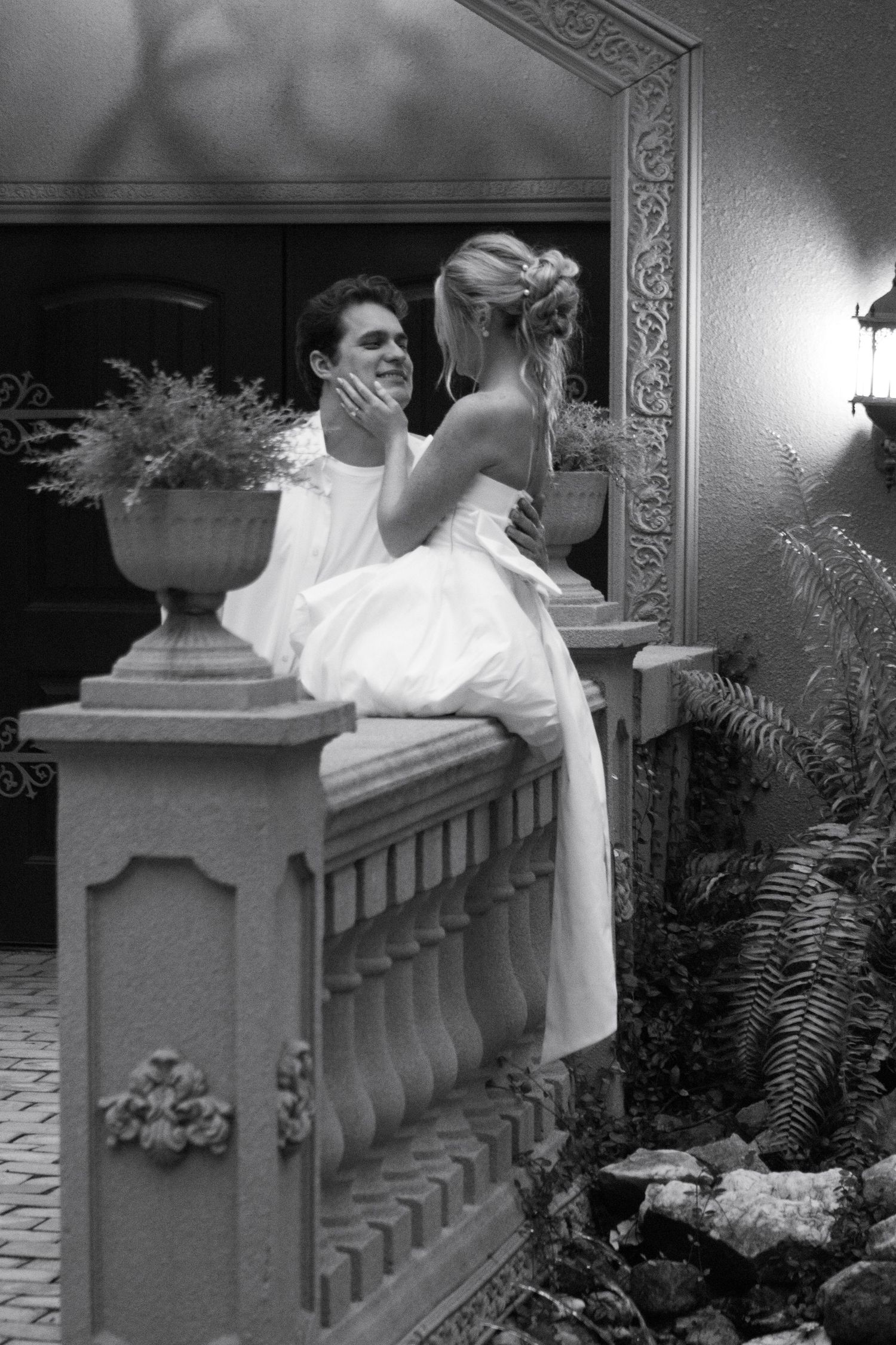 A couple shares a romantic moment on an ornate balcony in black and white.