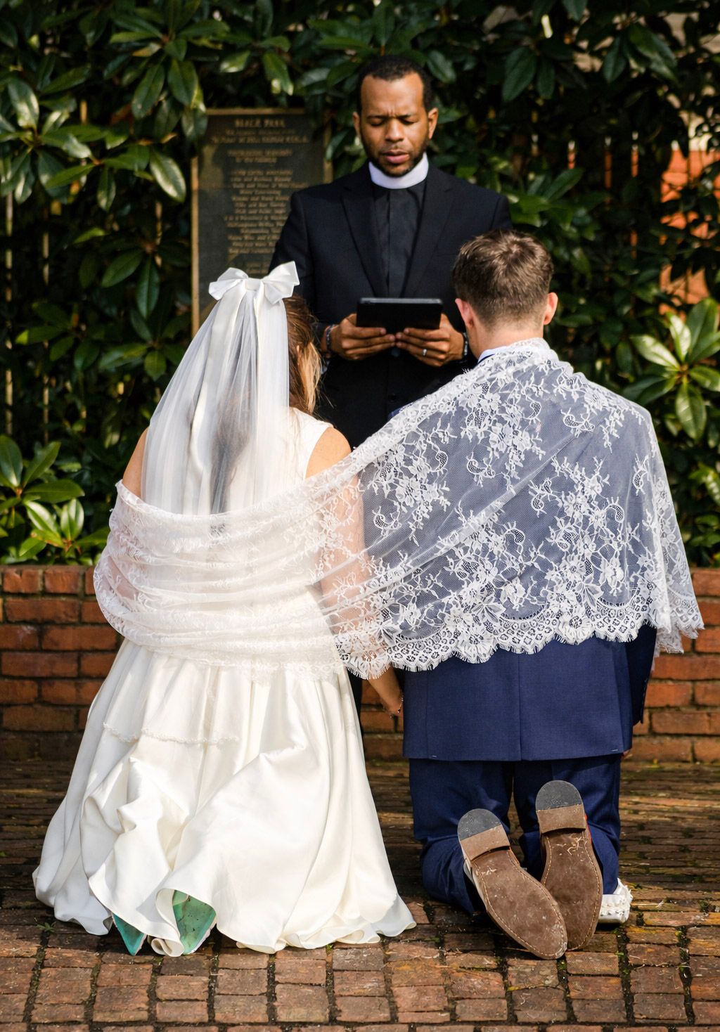 Close-up view of bride's lace veil and wedding dress details during outdoor ceremony on brick pathway.