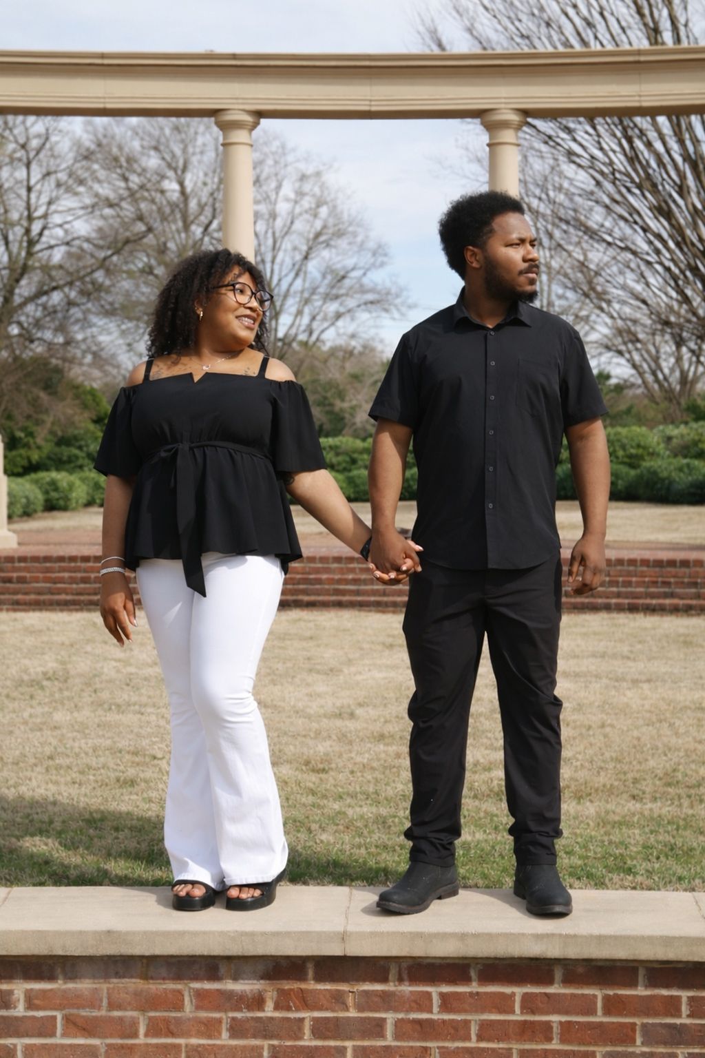 A couple in coordinating black and white outfits pose together on outdoor brick steps in a romantic photoshoot series.