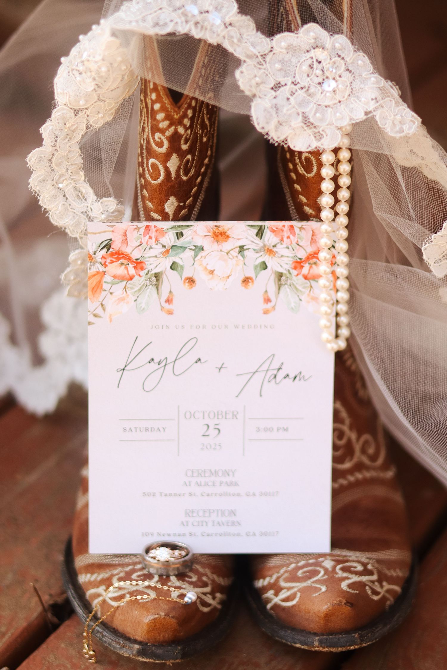 Brown leather cowboy boots with lace details and wedding invitation displayed against wooden surface.