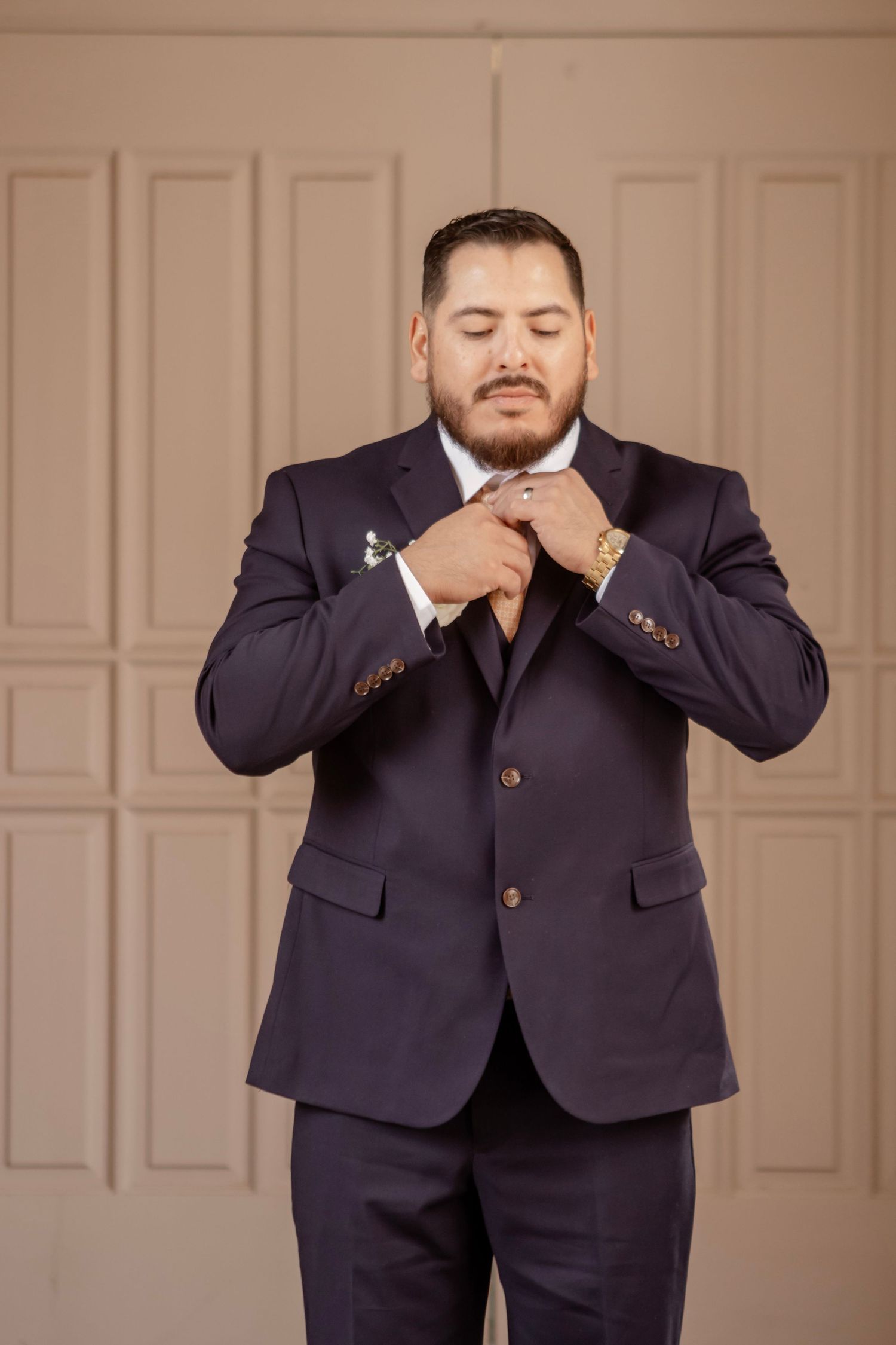 Man in navy suit jacket makes playful poses against beige wall in professional photo series.