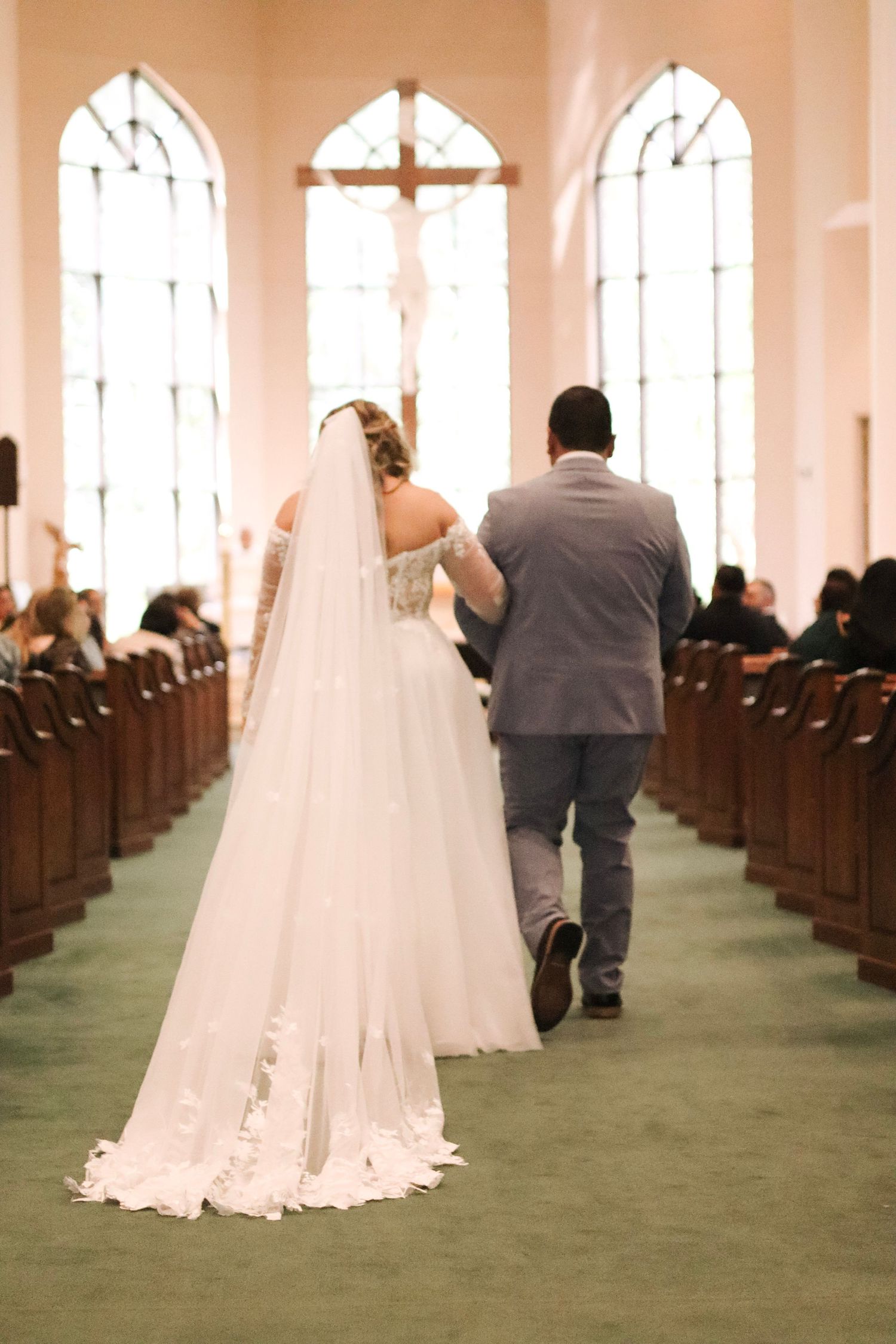 Wedding ceremony in a church with arched windows and green carpet aisle.