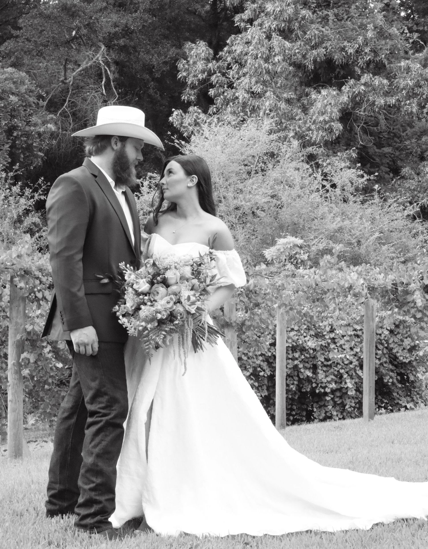 Black and white panoramic wedding portraits in garden setting with white dress trailing on grass.