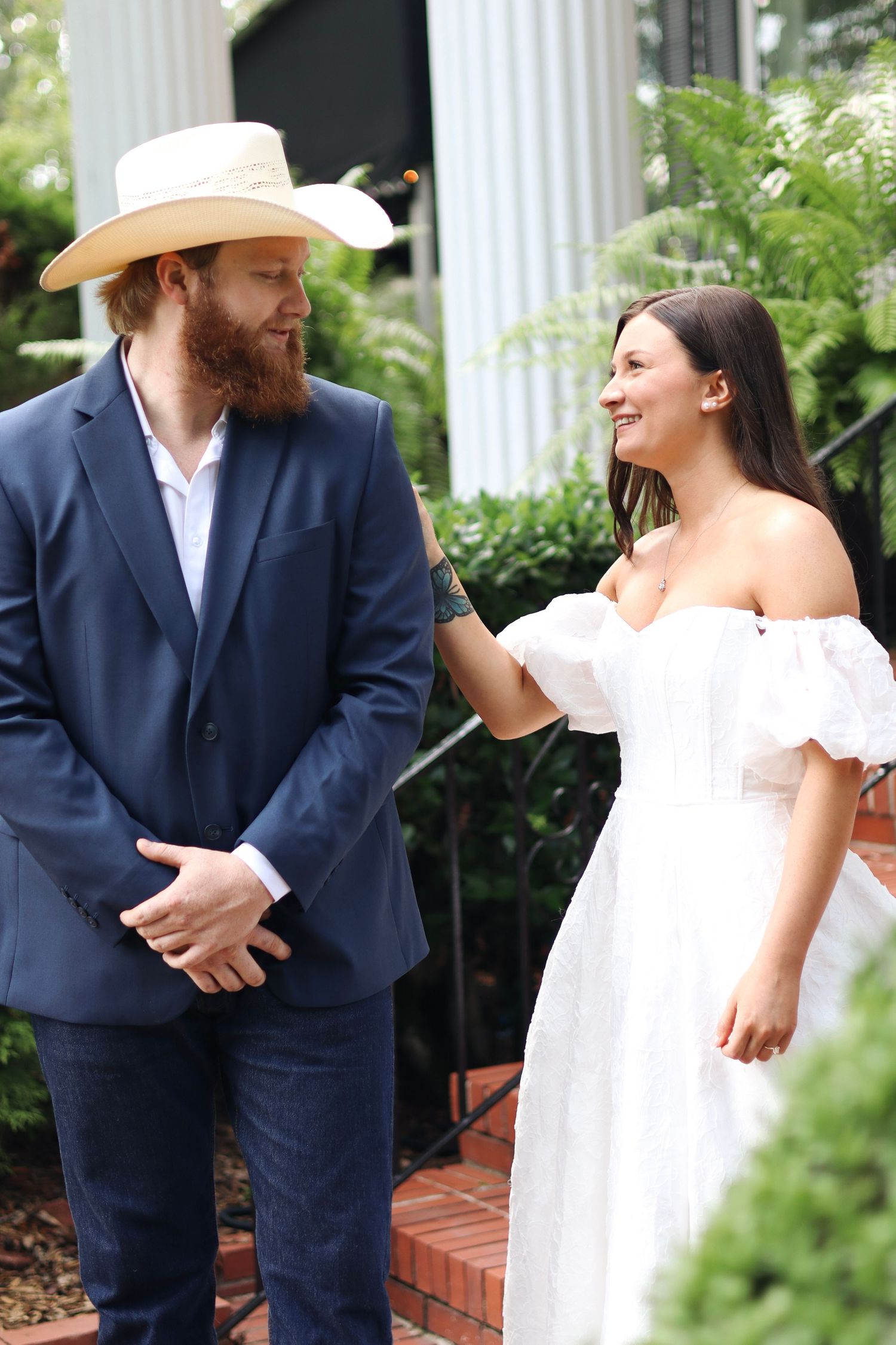 A joyful moment between two people, one in a navy suit and cowboy hat, the other in a white dress.