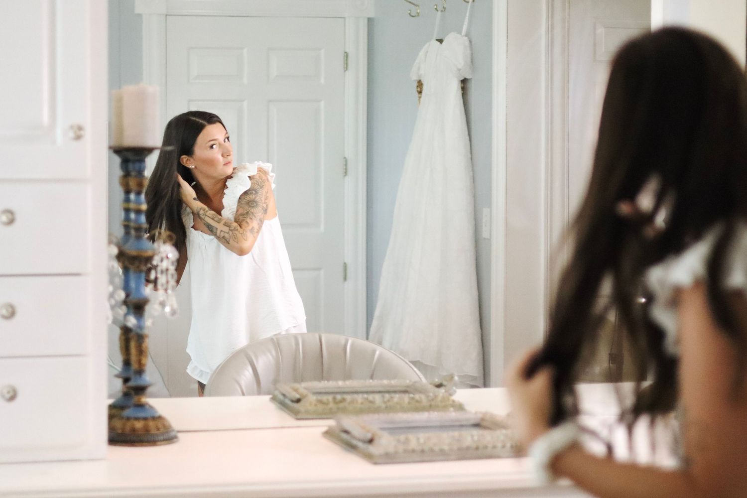 Reflections in a mirror show a bride getting ready in a bright white room.