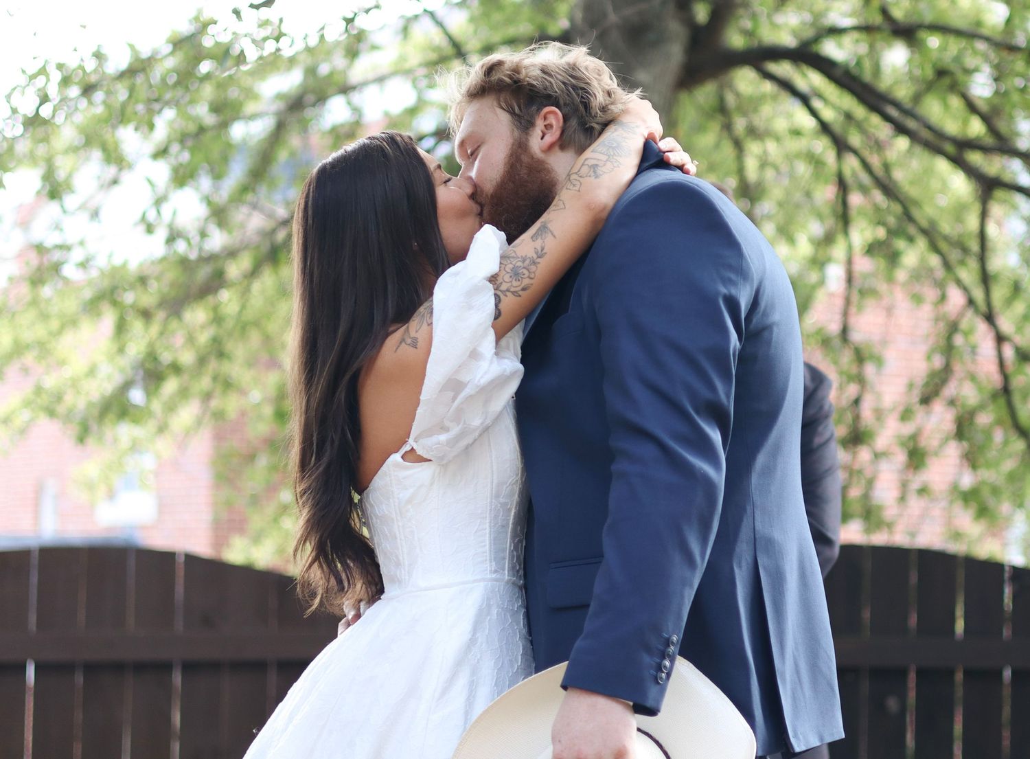 A romantic outdoor wedding scene with a couple embracing under trees.