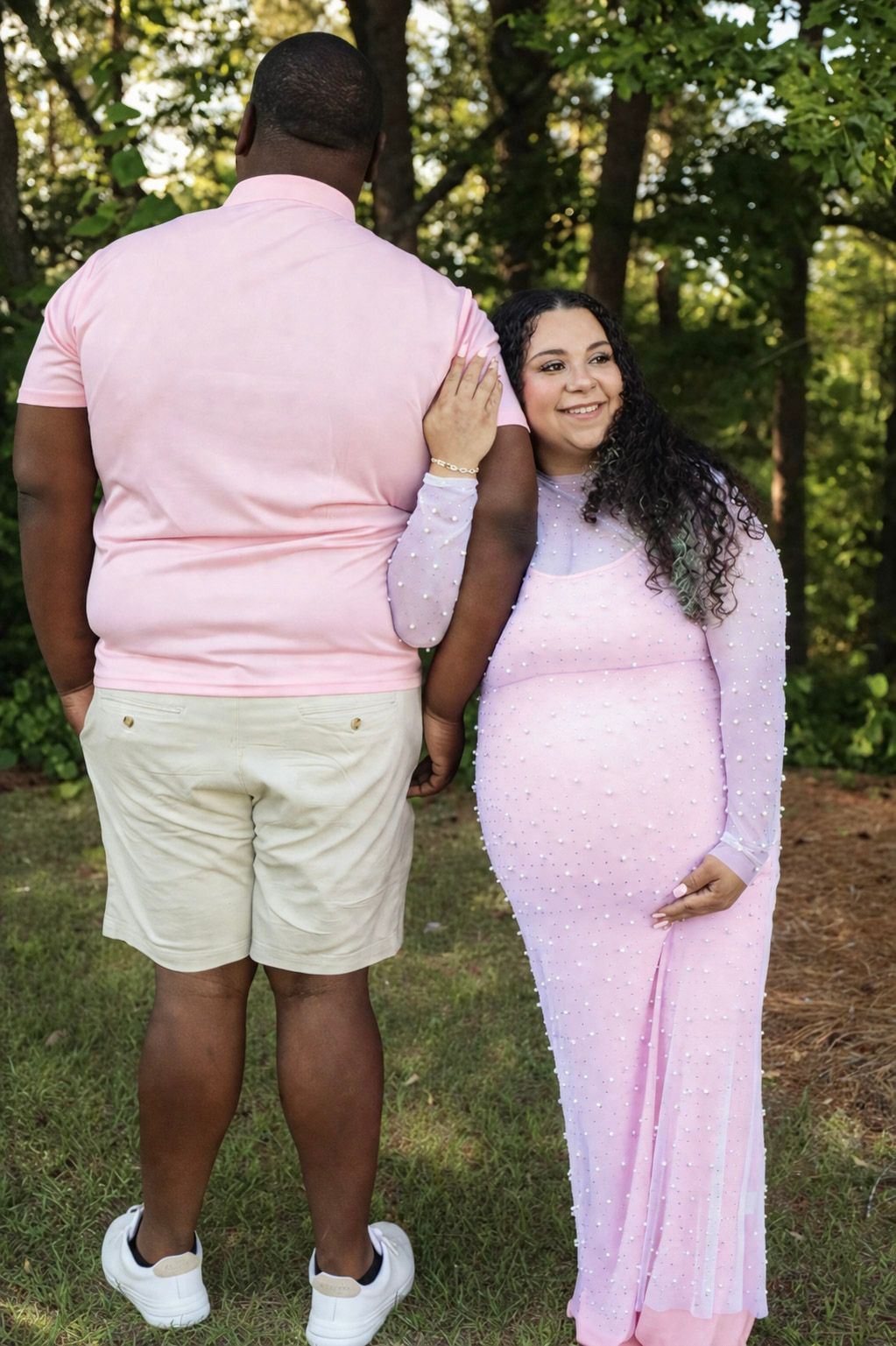 A pregnant woman in a pink sequin gown poses with her partner outdoors during a maternity photoshoot.