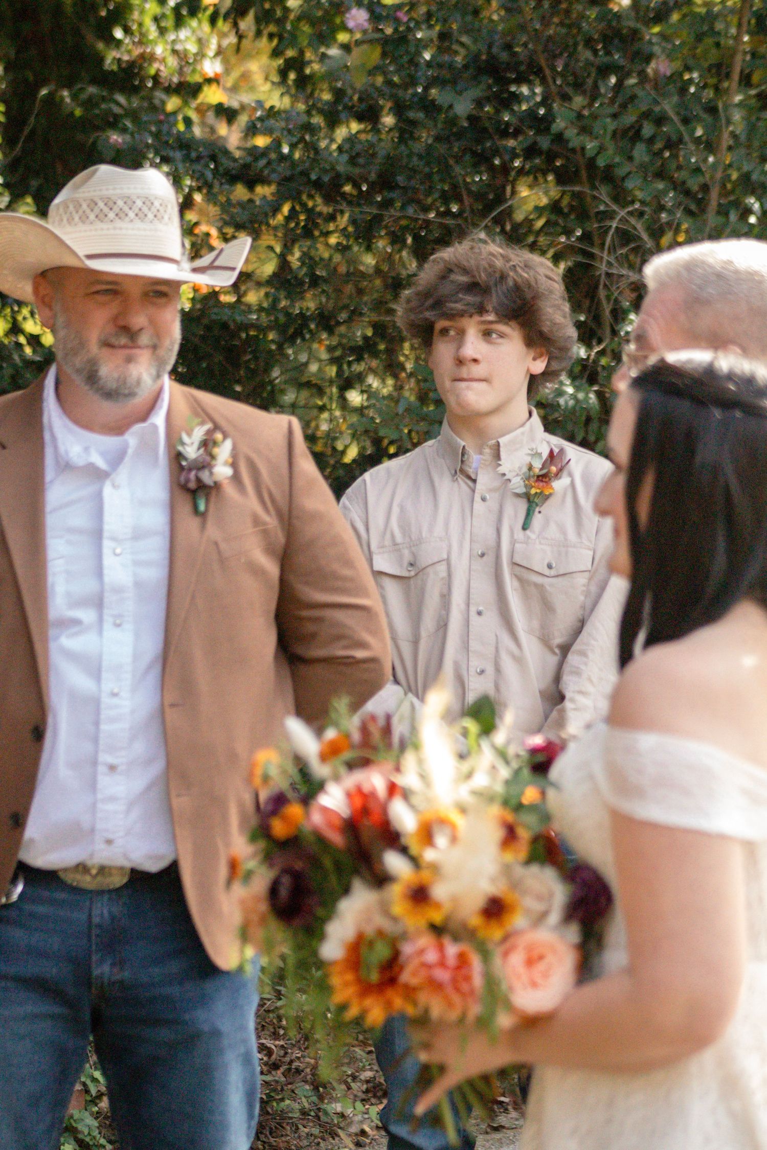 A rustic country wedding scene with brown and white attire and colorful autumn floral bouquets in an outdoor setting.
