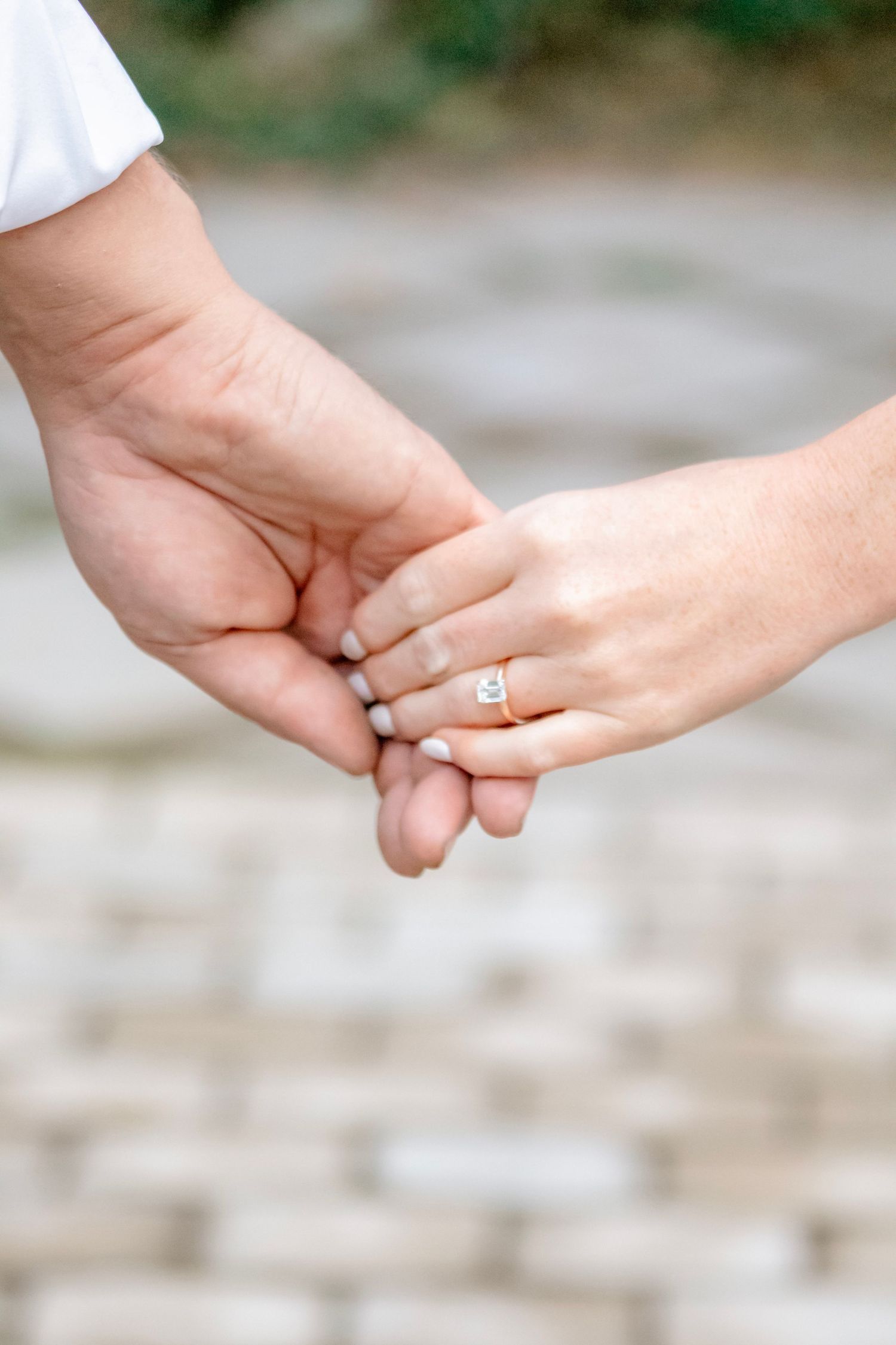 Close-up of clasped hands showing an engagement ring against a stone background.