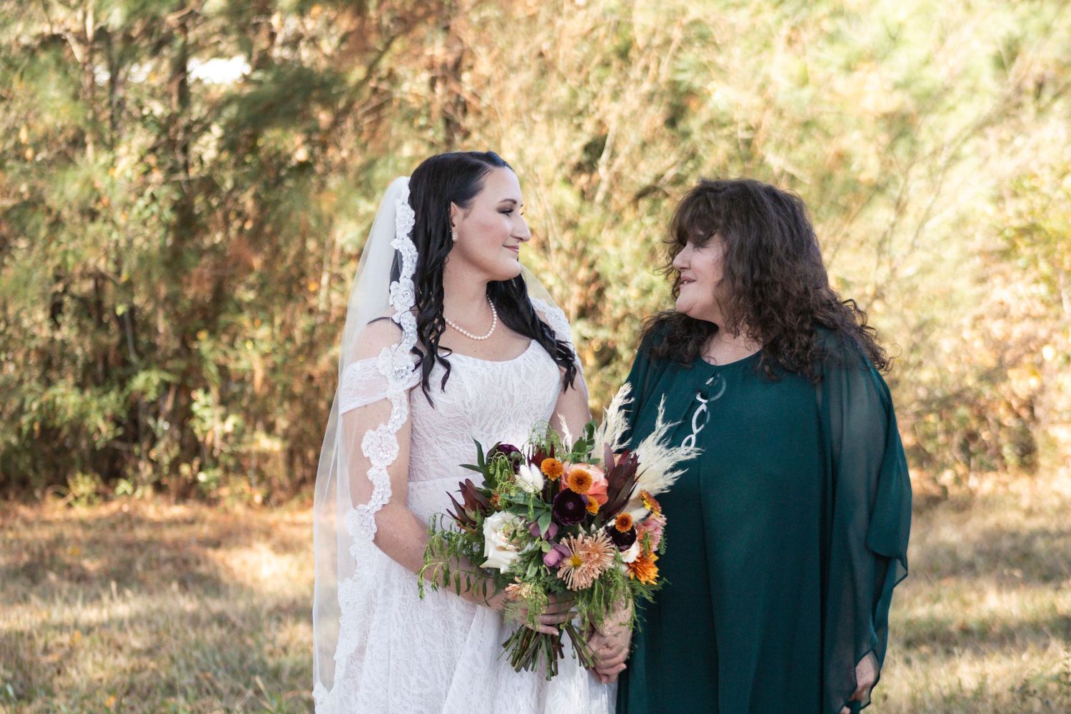 Two people in wedding attire share joyful moments in a sunlit outdoor setting with autumn foliage in the background.