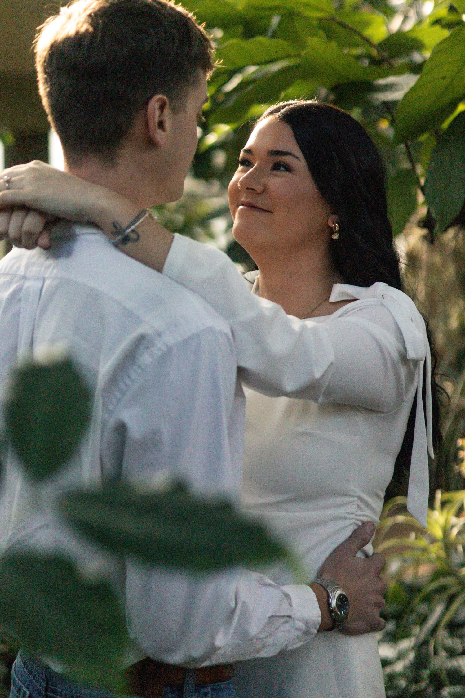 A couple in white attire share an intimate moment in a garden setting.