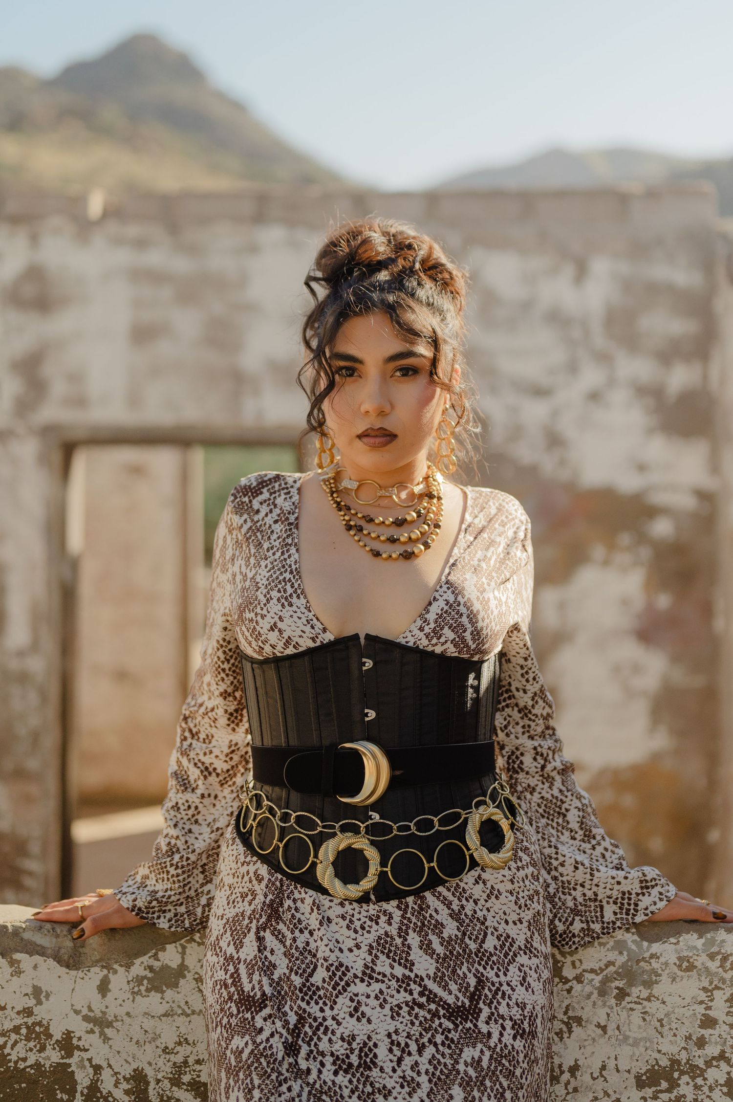 Fashion portrait of a woman in a belted corset dress, standing confidently in the desert ruins.