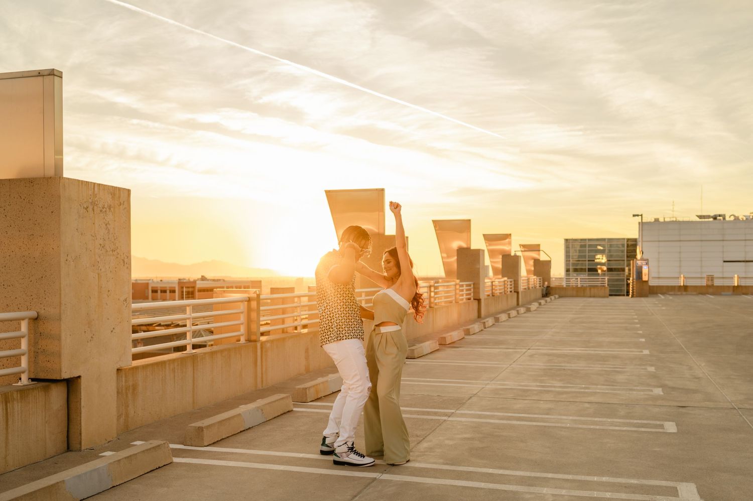 Couple embracing on rooftop parking lot at golden sunset, romantic engagement photo with warm glowing sky.