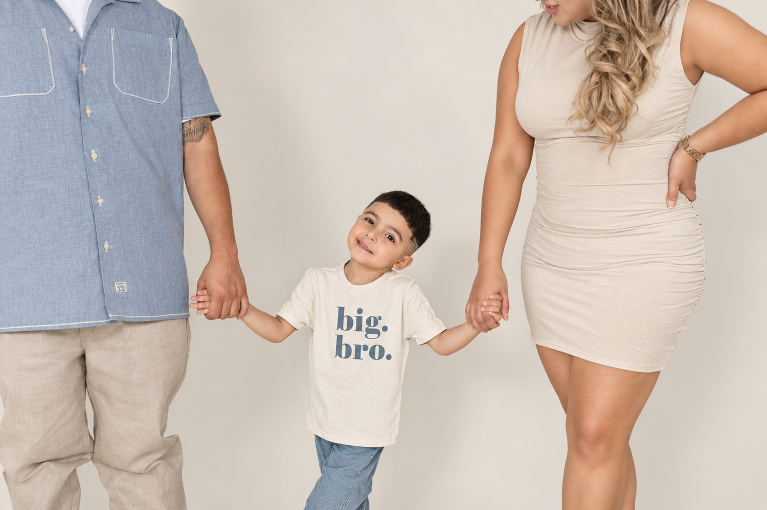 smiling toddler in a big bro tee holding hands with mom and dad, big brother pregnancy announcement photo in phoenix