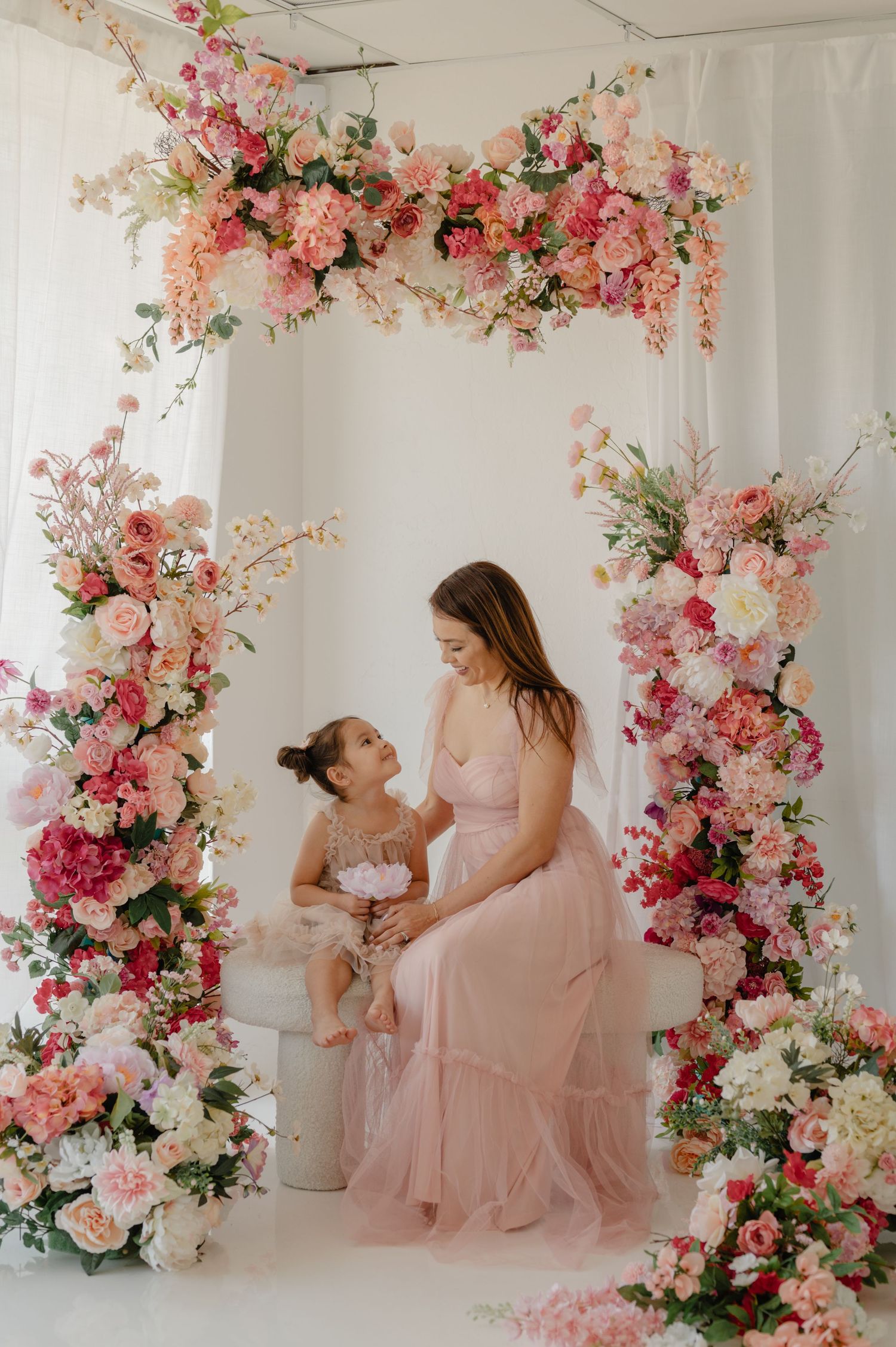 mom in a pink gown smiling at her daughter surrounded by a floral arch, mommy and me photography session in glendale