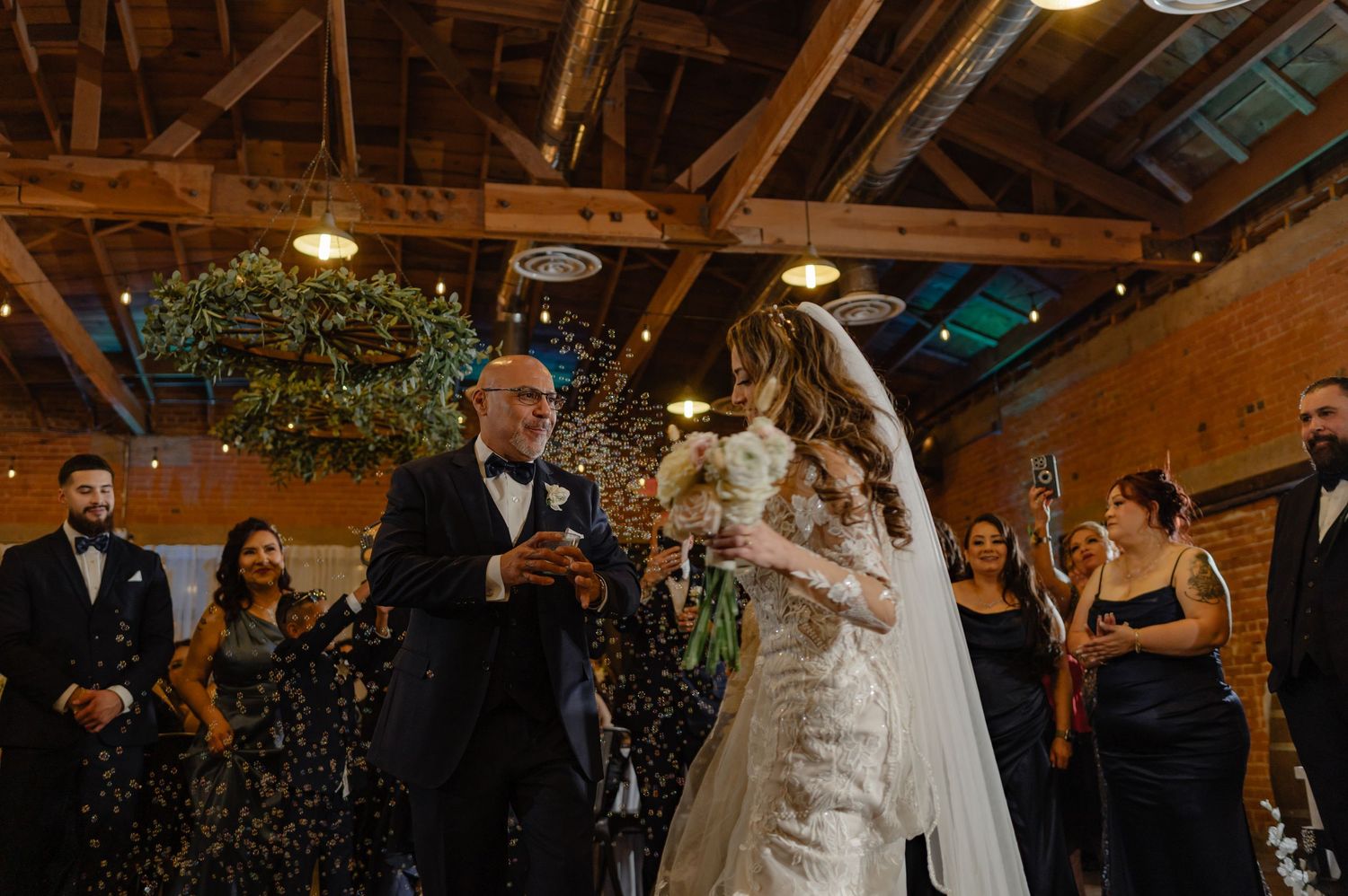 Just married couple exiting ceremony, confetti in the air, surrounded by guests in a cozy indoor wedding setting.