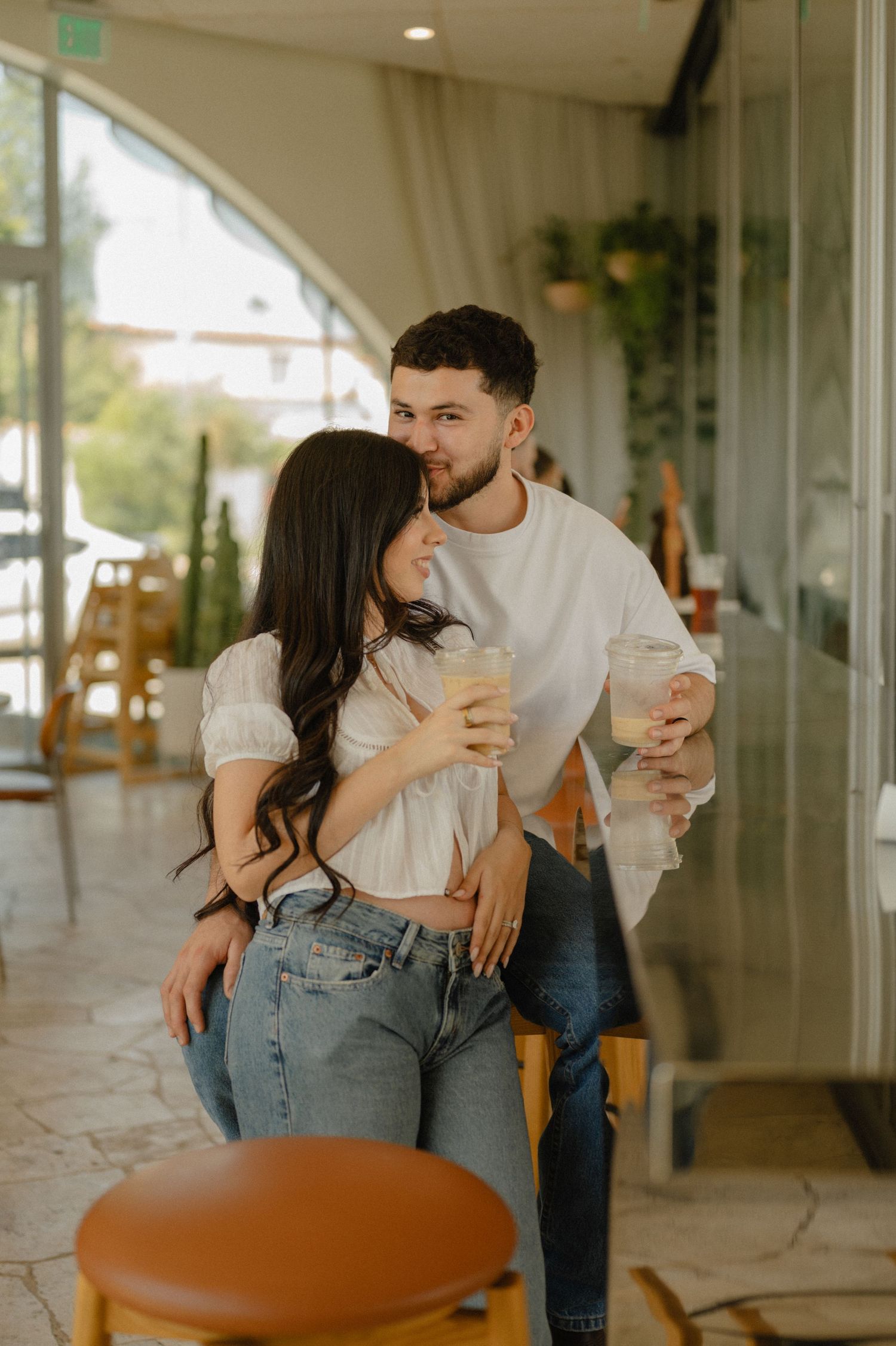 couple holds iced coffees and laughs together at sophia's brunch counter during a phoenix pregnancy announcement session