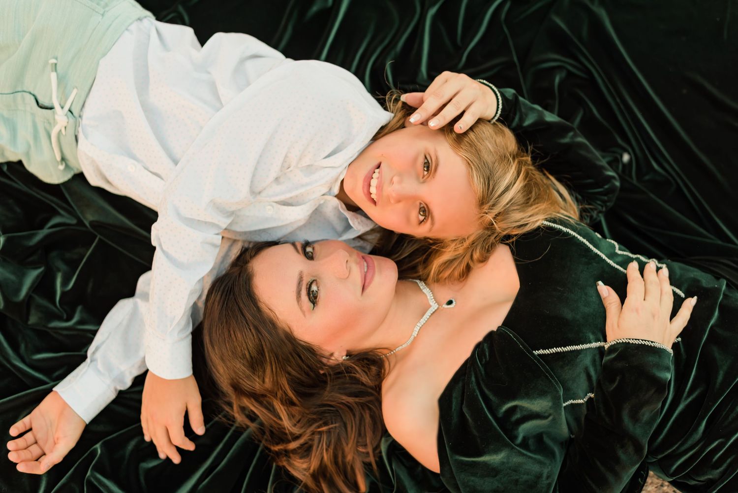 Two friends lie together on dark green velvet, smiling in a portrait session in downtown Phoenix, AZ.
