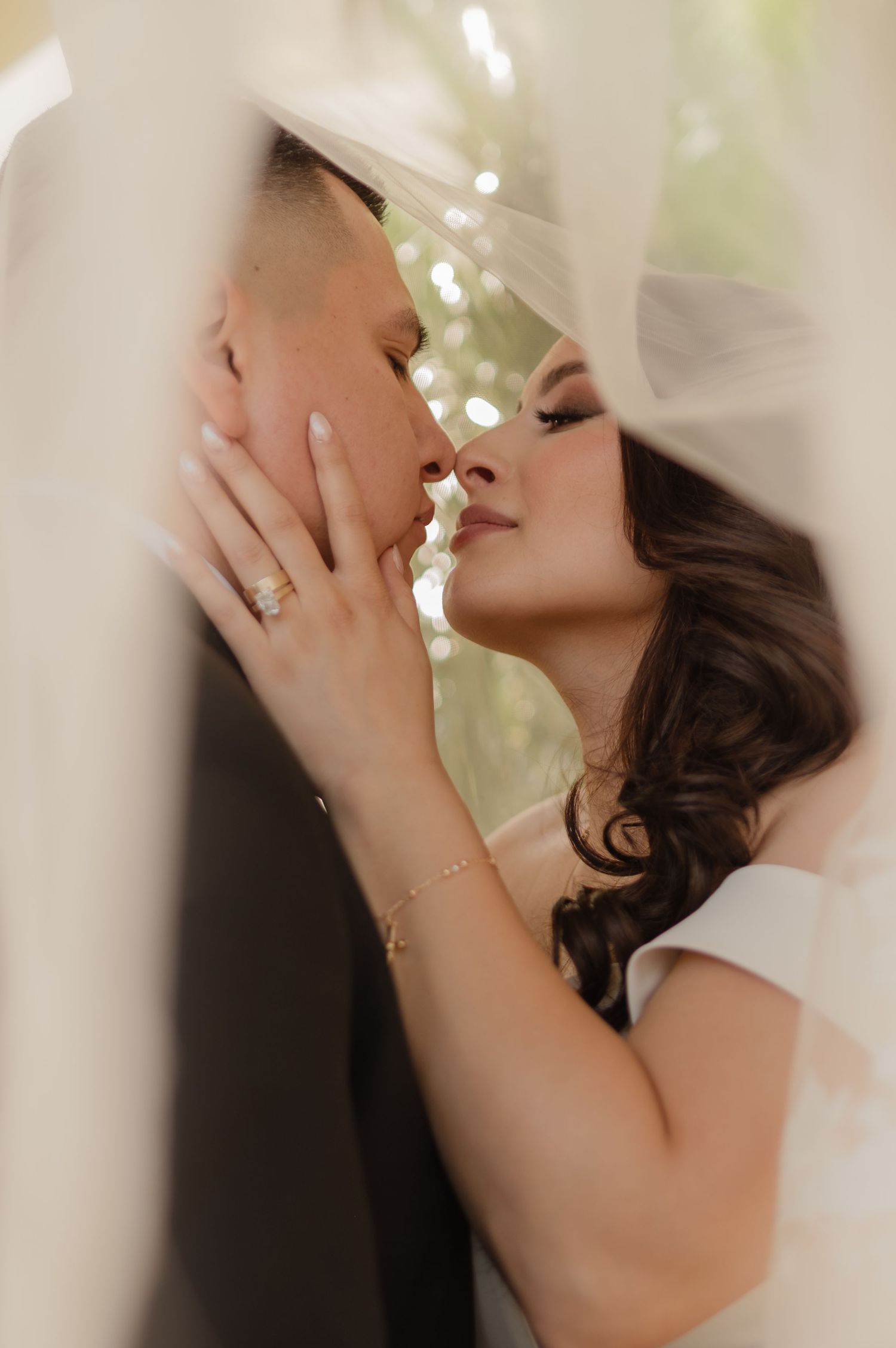 Bride and groom share intimate kiss under veil, close-up with soft romantic lighting.