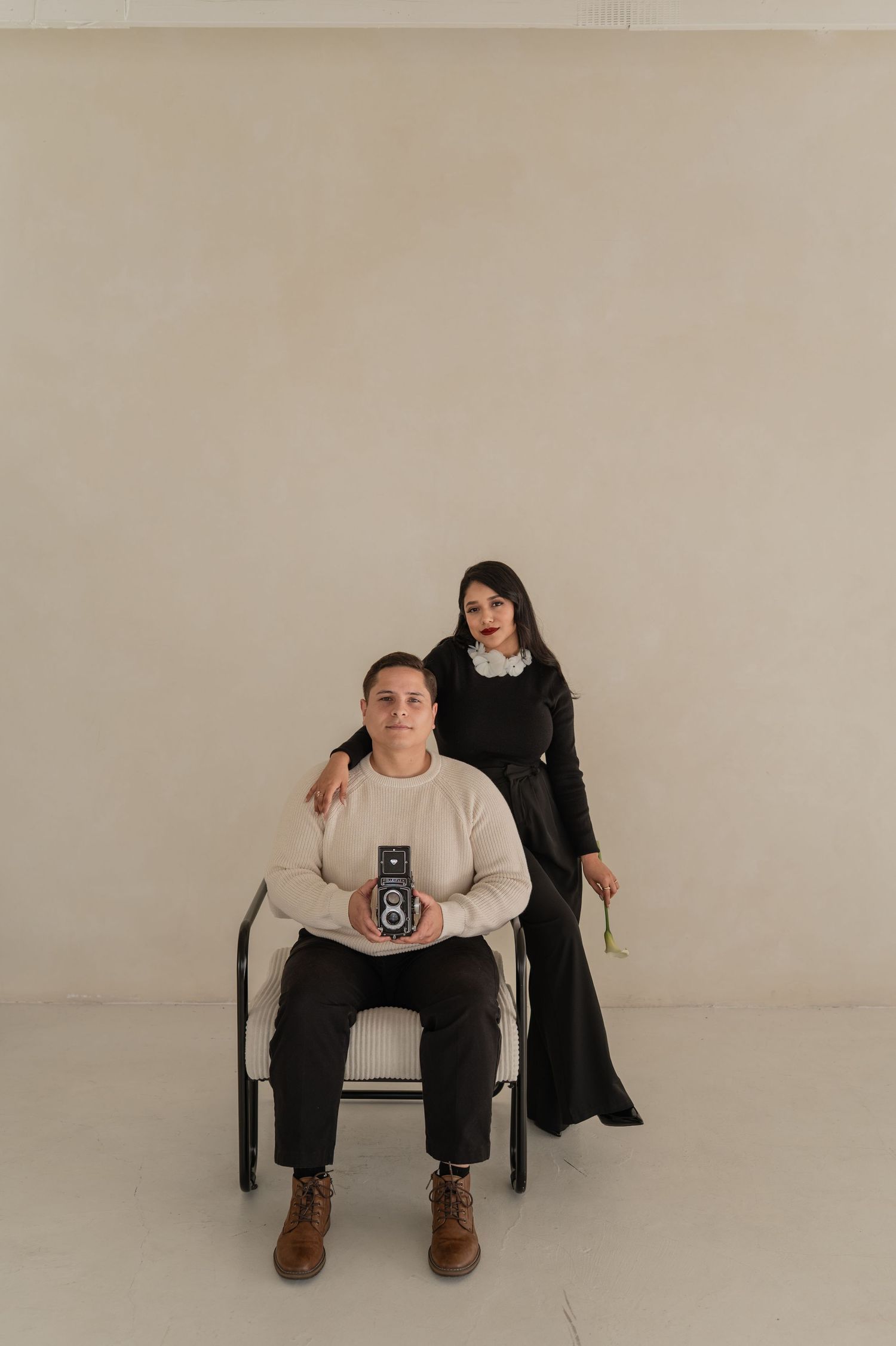 Studio portrait of a man sitting on a stool with a woman standing behind — creative duo branding.