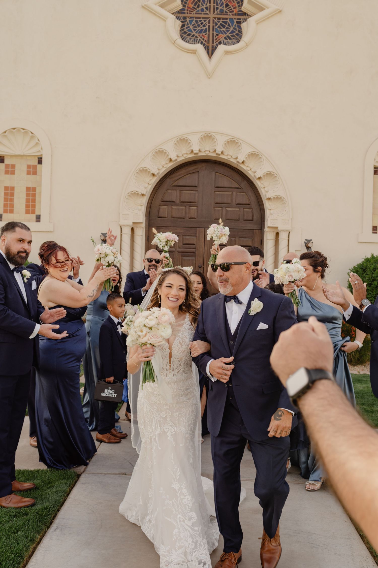 Bride and groom exit ceremony surrounded by cheering guests and flower petals.