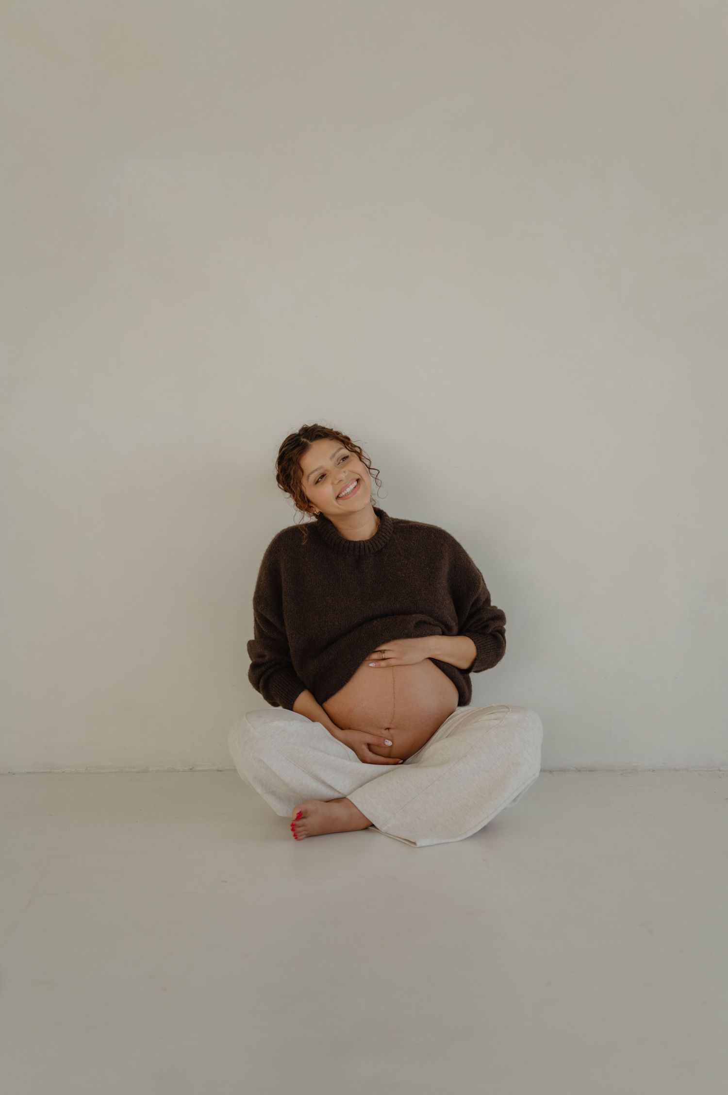 pregnant woman sits cross legged holding her bump during a phoenix studio maternity session