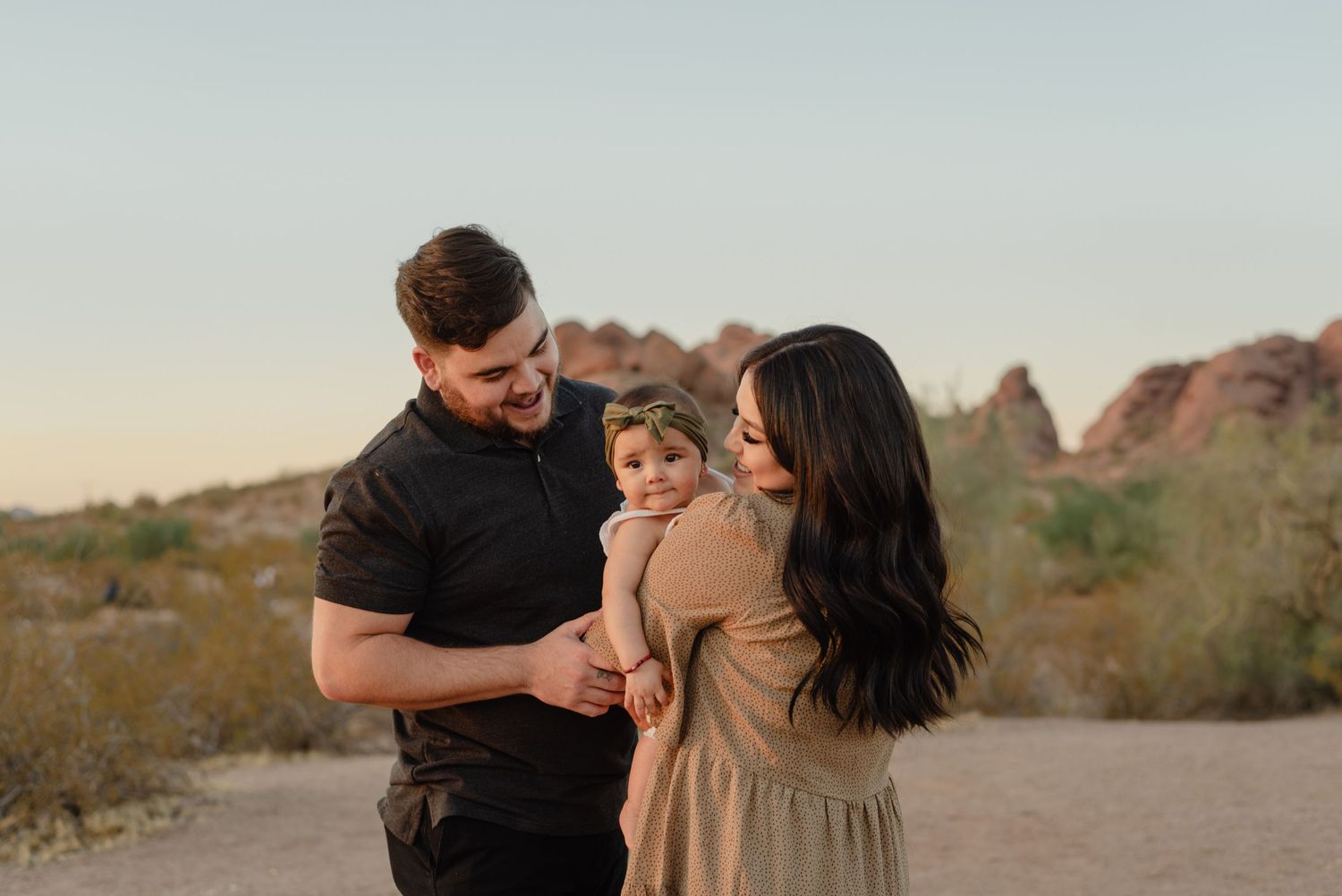A young family with a baby poses in a desert landscape with red rock formations at golden hour.