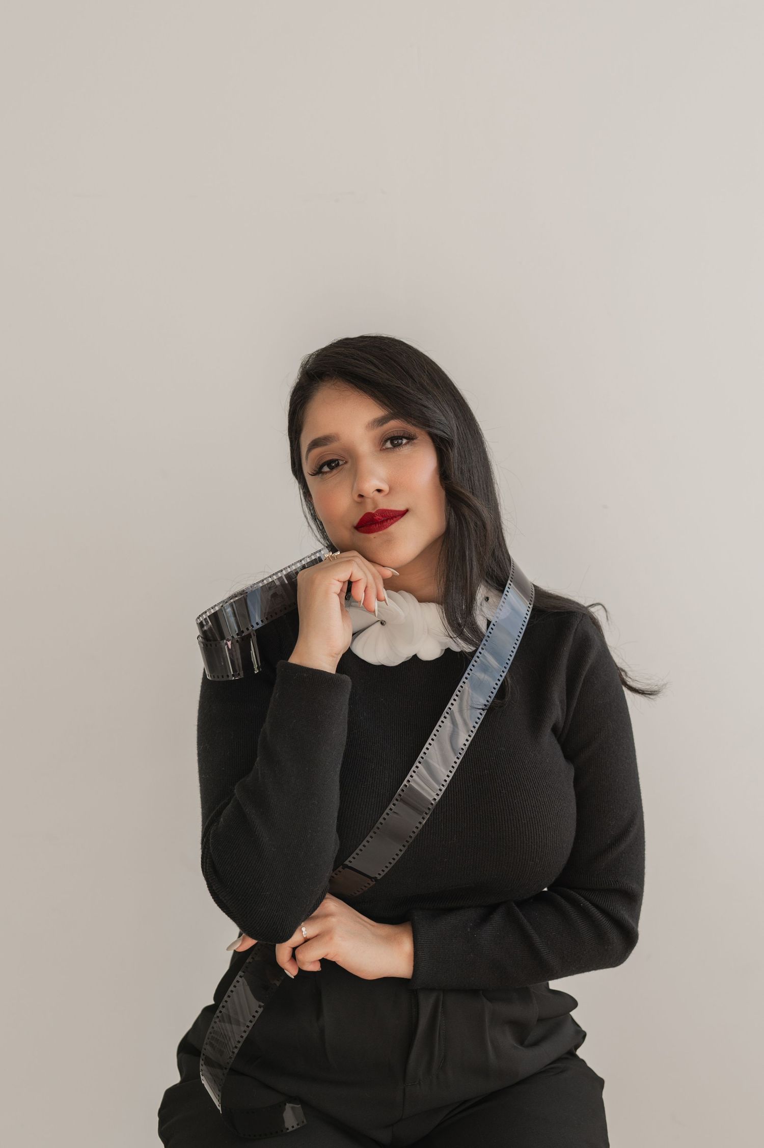 Woman in black posing confidently with a camera — clean studio branding portrait.