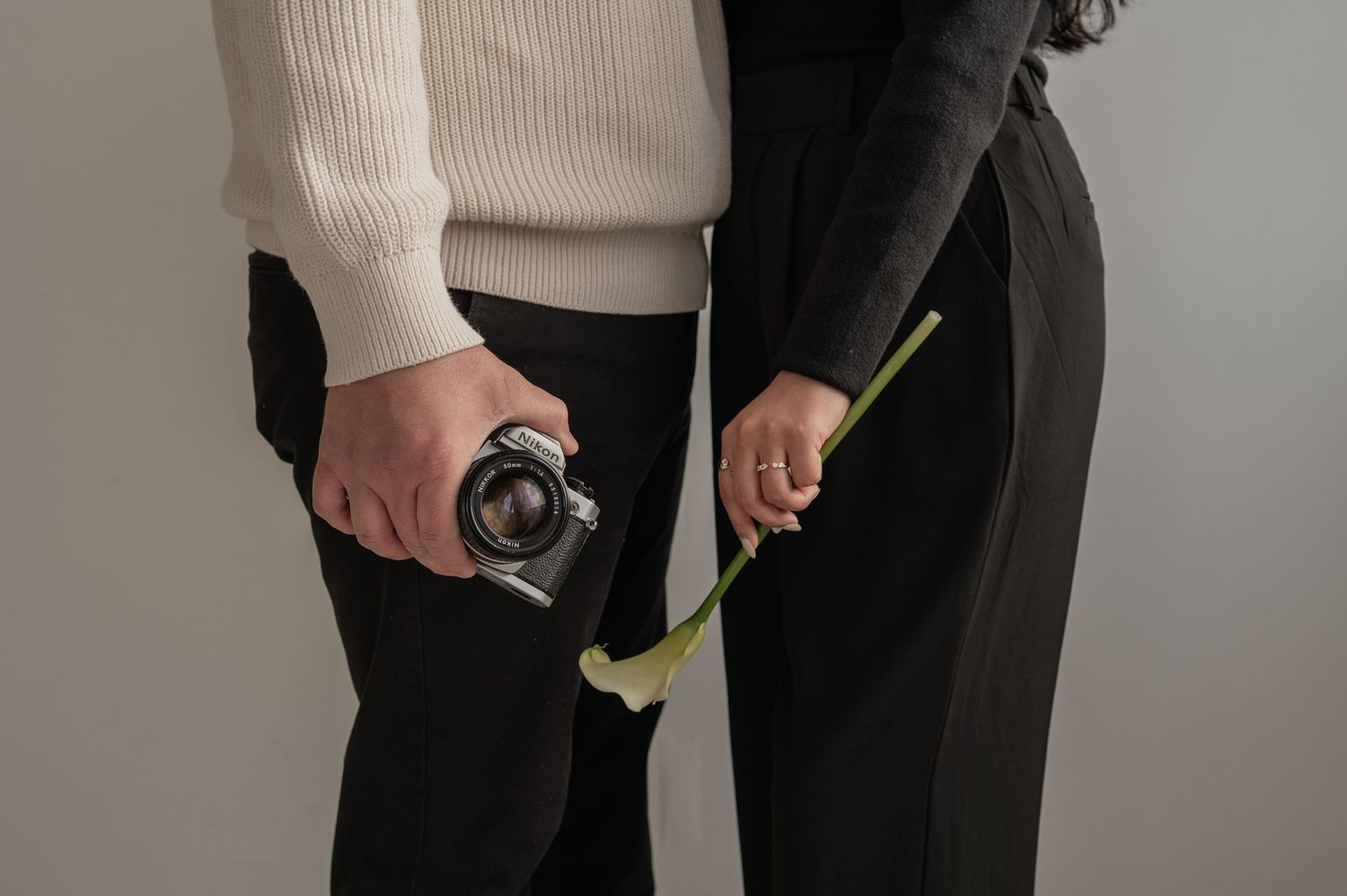 Minimalist shot of a man and woman holding cameras and florals, shown from the waist down — clean, editorial styling.