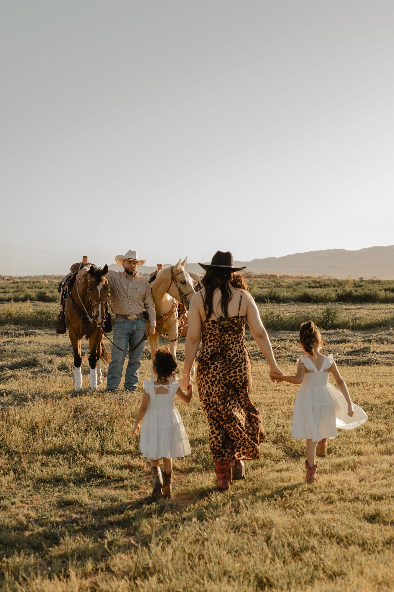 A mother in a leopard print dress and cowboy hat walks hand in hand with her daughters toward a horse in Glendale, AZ.
