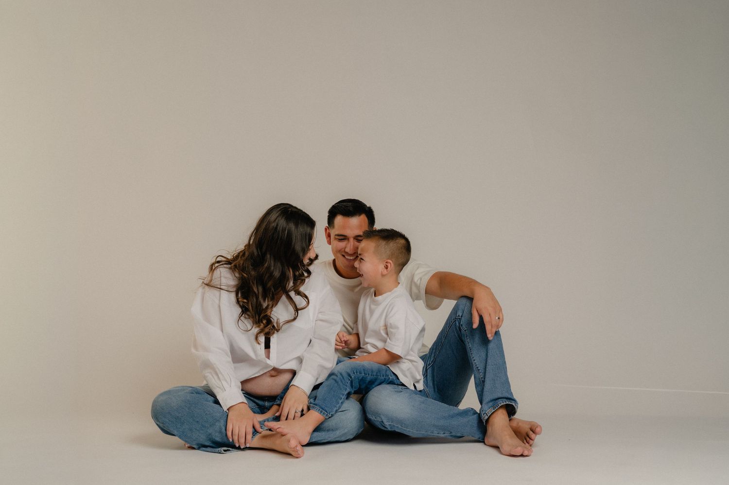 family sits together on the floor during a phoenix studio maternity session, mom cradling her bump