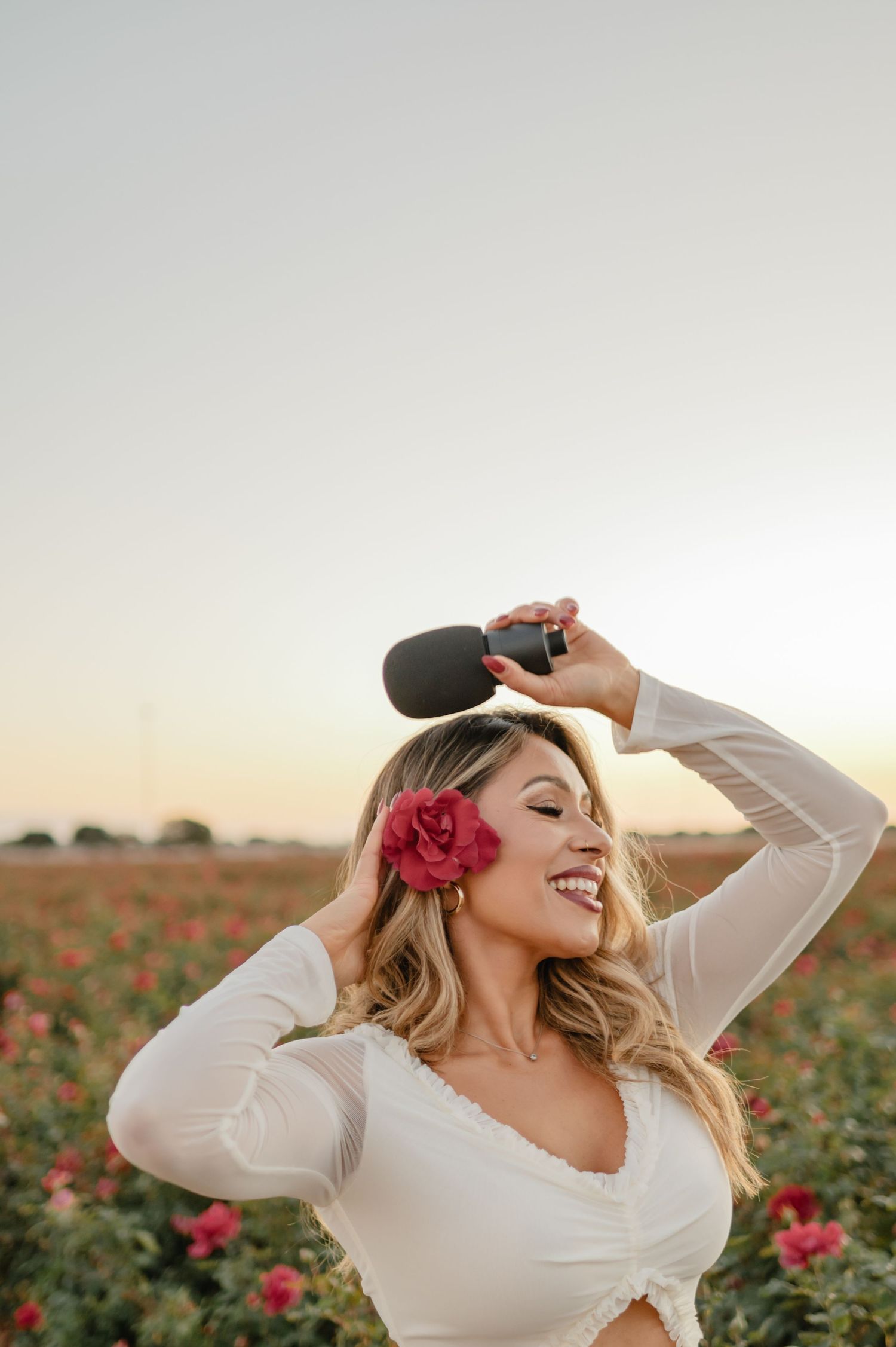 Rosy Liddi, wellness and business coach, founder of Calma Wellness Lounge, smiling in a blooming rose field at sunset.