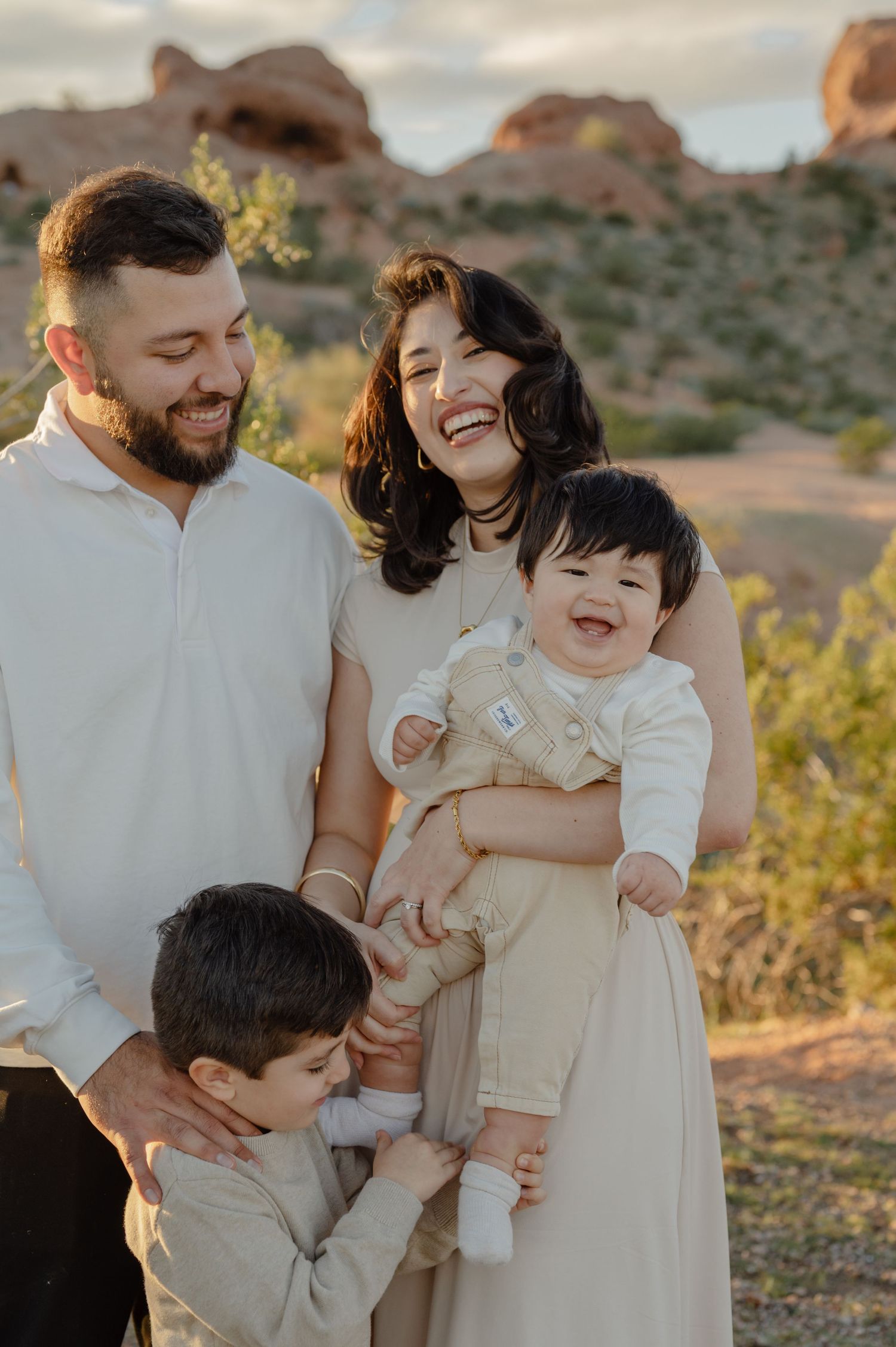 Joyful family of four laughing together outdoors with red rock formations in a desert landscape at golden hour.