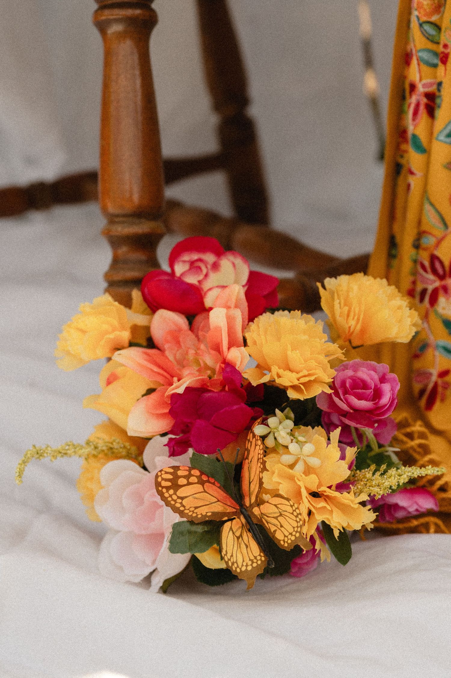 Colorful floral arrangement with yellow, pink roses and monarch butterfly near wooden chair.