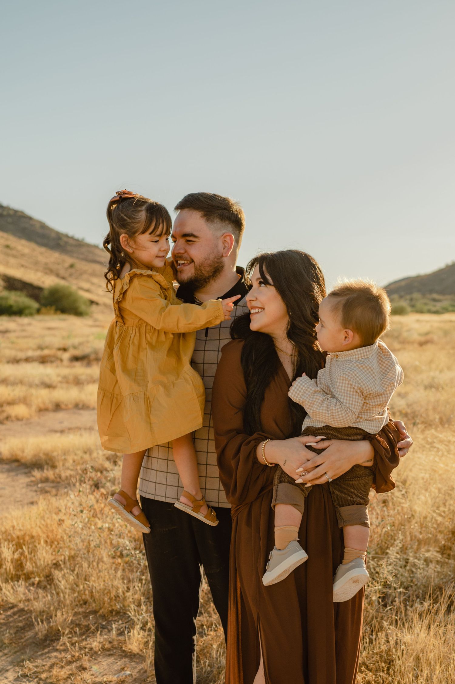 Happy family of four with two young children embracing in golden desert field at sunset.
