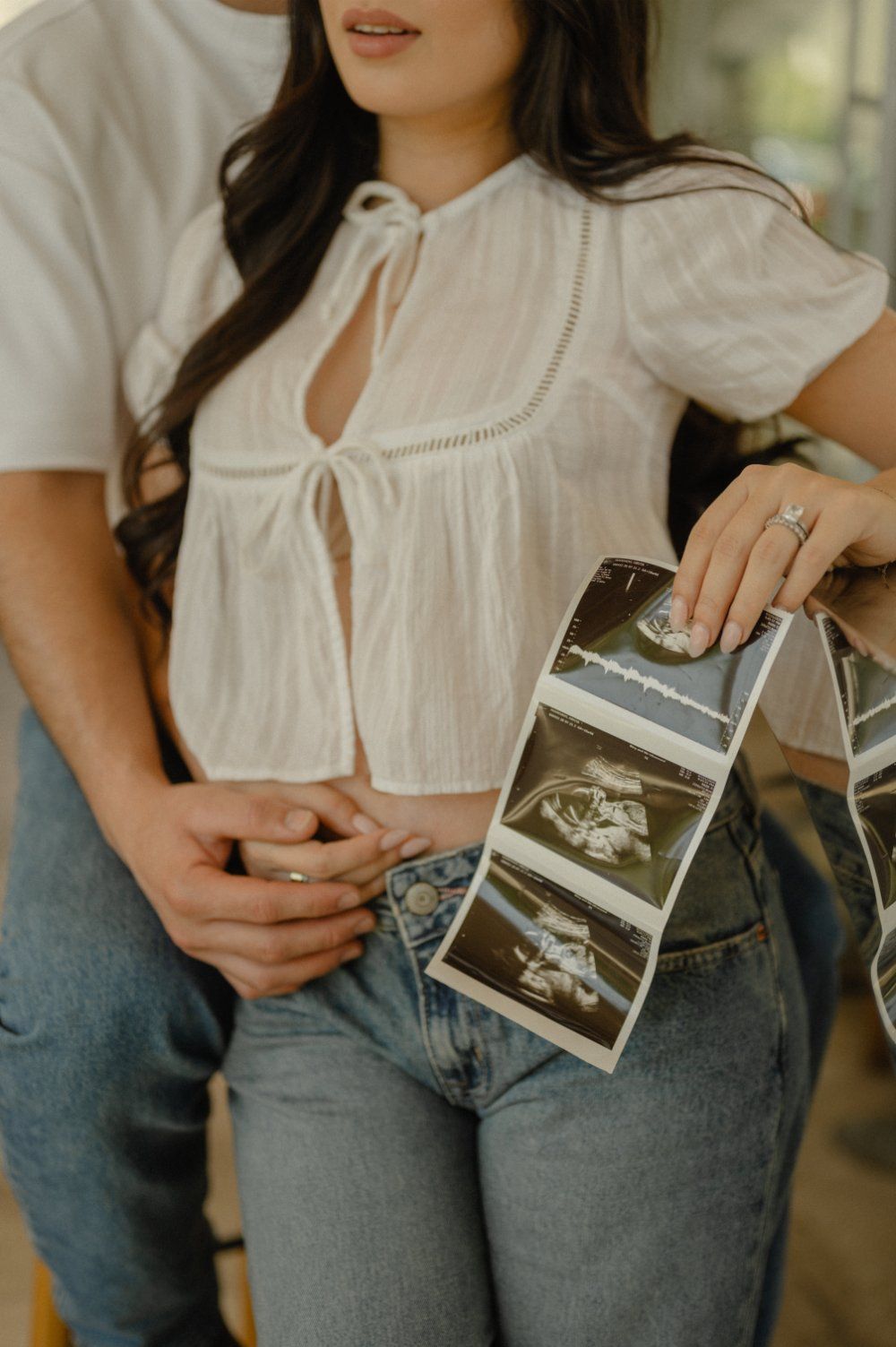 Close up of a couple holding hands with their sonogram strip tucked against jeans