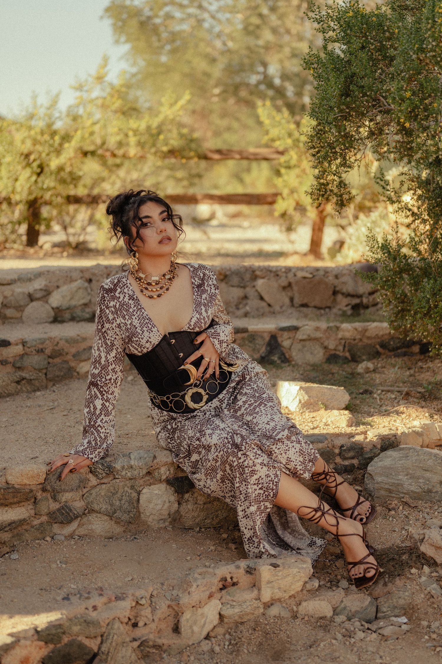Stylish woman sits on desert rocks in sunset light, wearing animal print and chunky belt.