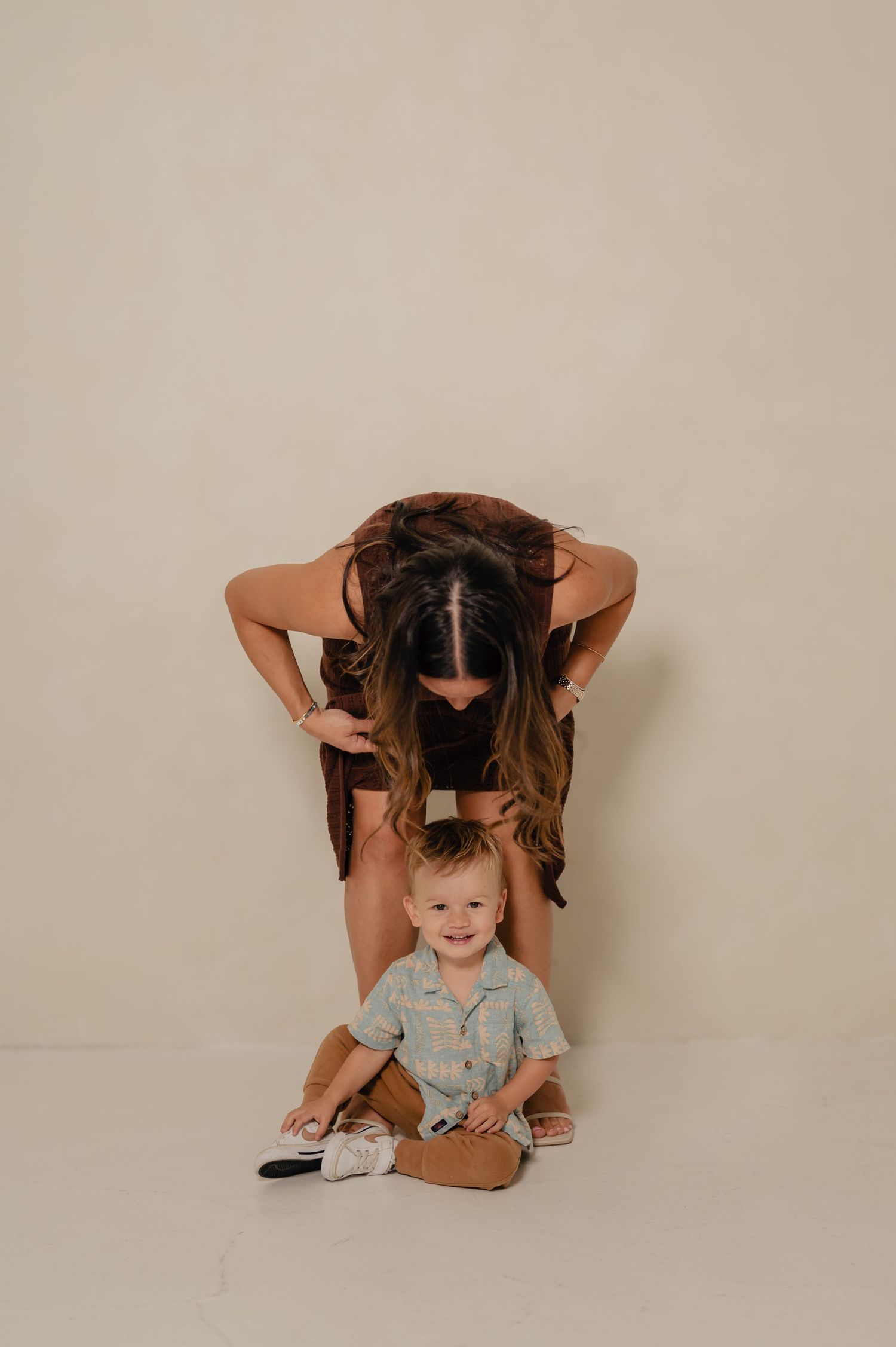 A mother leans over her smiling blonde toddler during a studio portrait session at Refine Studios in Phoenix, AZ.