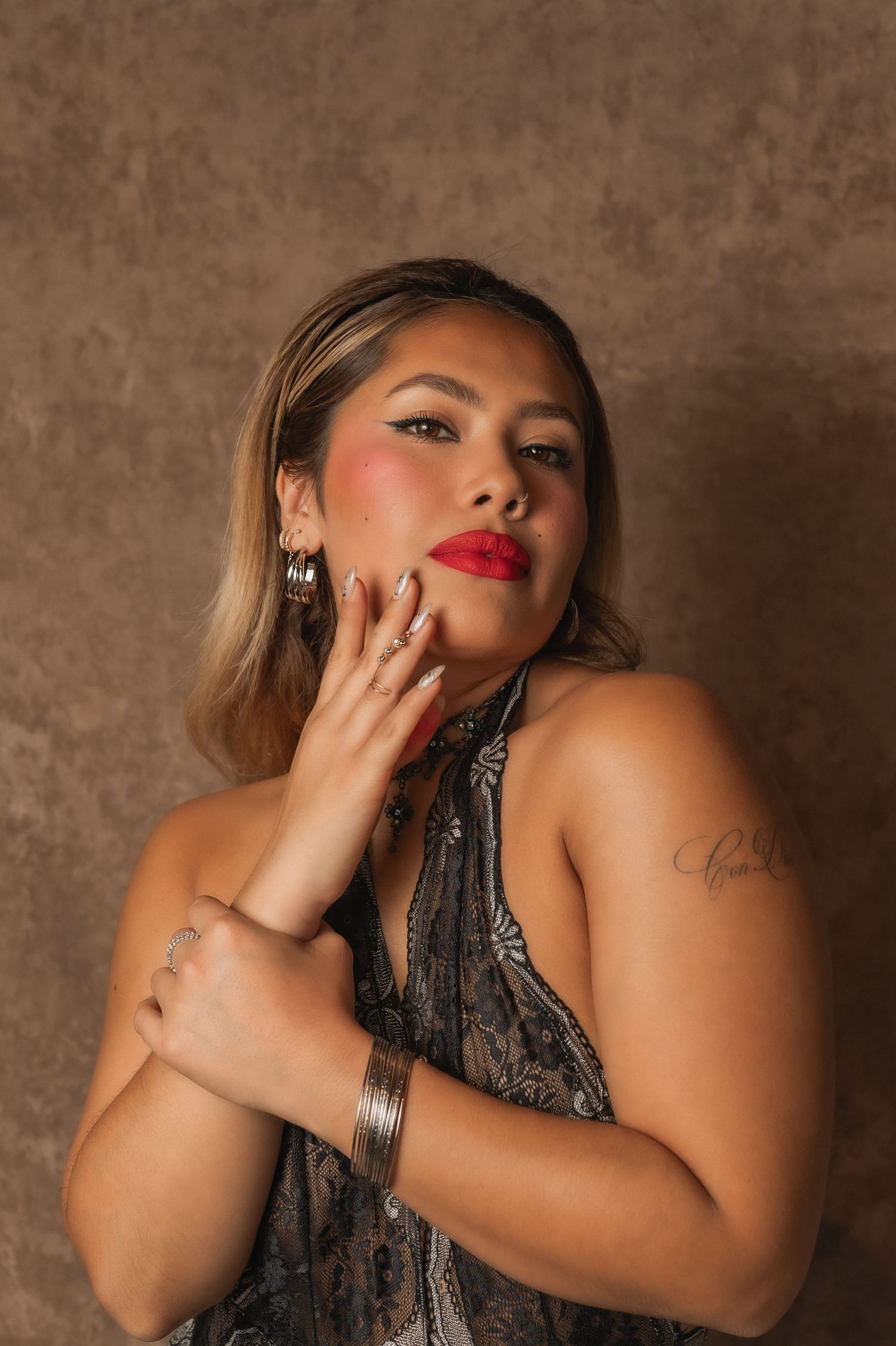 Woman in a halter dress with bold makeup poses with elegance against a brown studio backdrop.