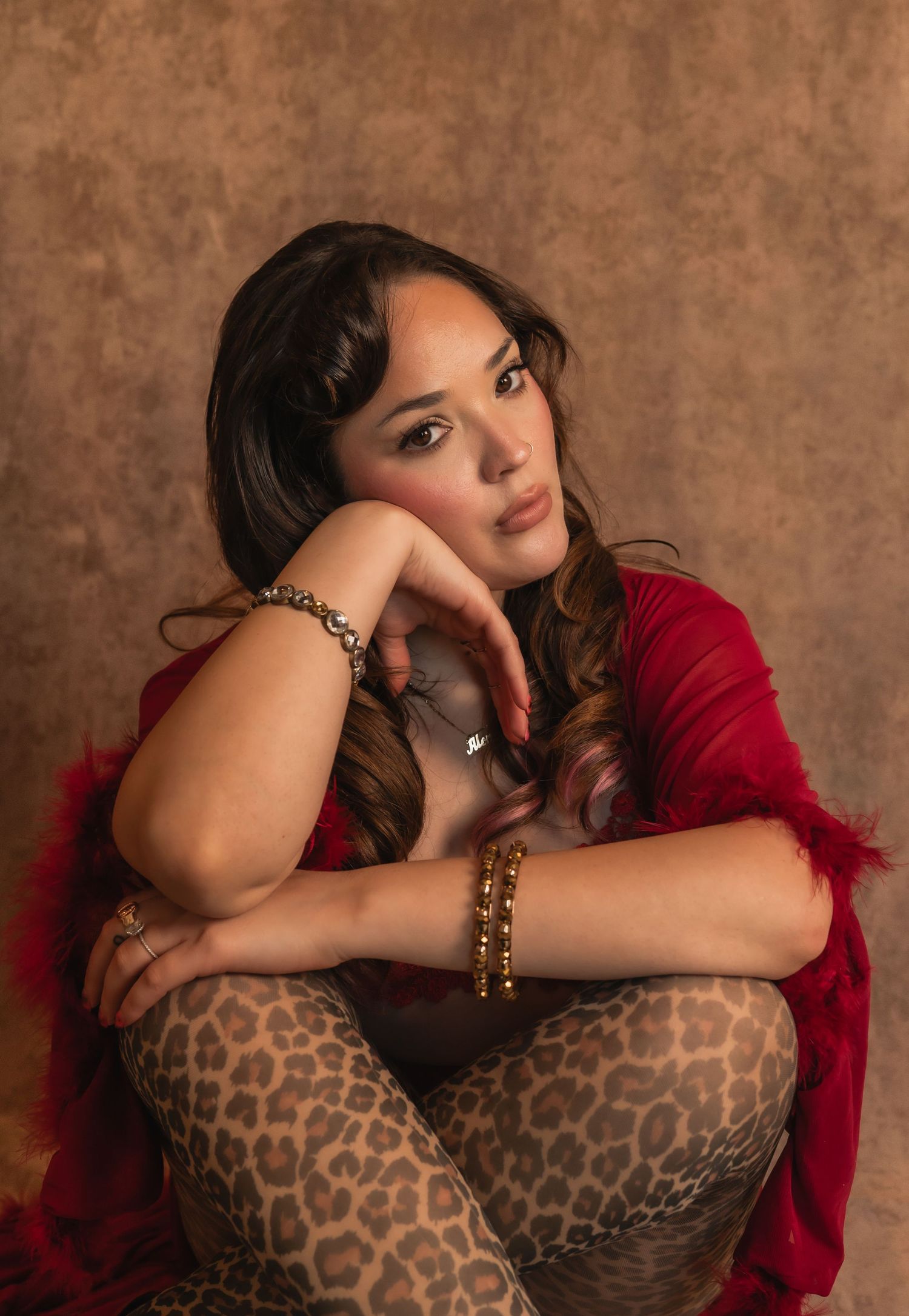 Woman in red top and leopard pants rests her head on her hand with a thoughtful gaze.