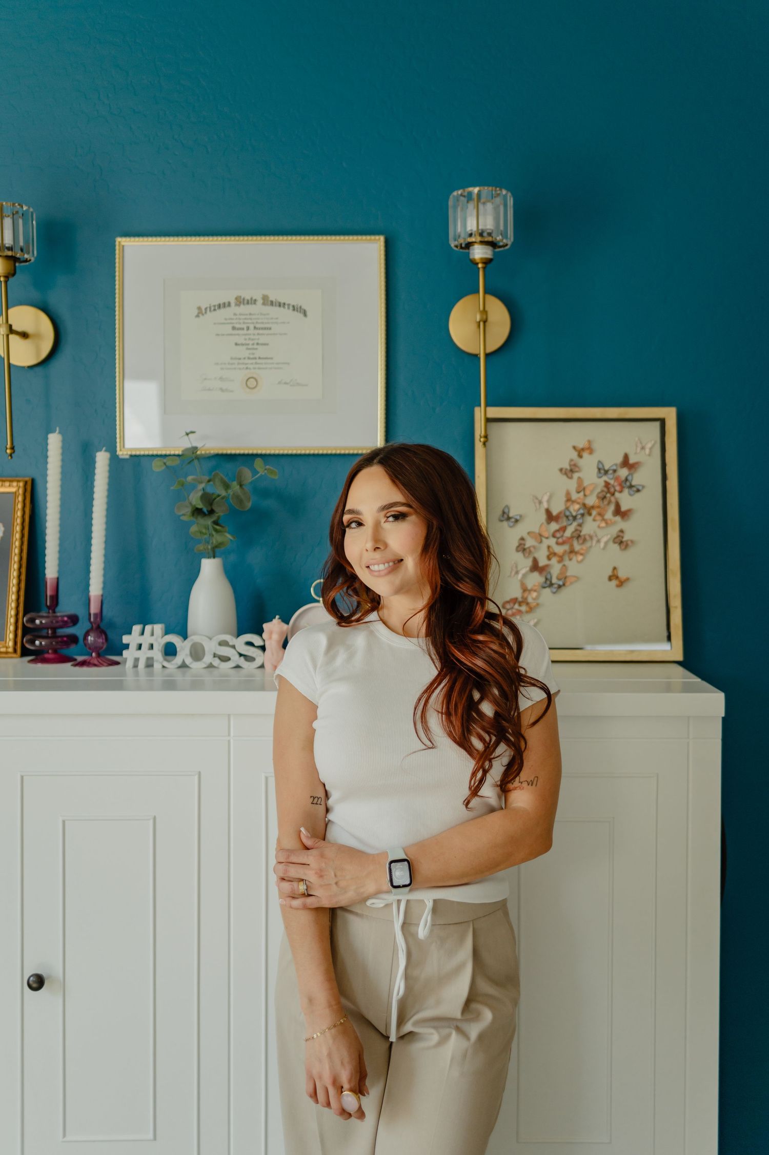 Diana standing confidently in front of a teal wall with framed art — branding and personality-forward portrait.