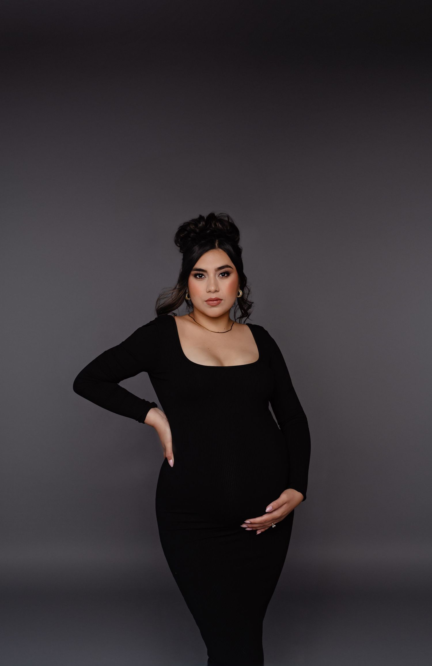 pregnant woman in a black gown poses against a dark studio backdrop in phoenix